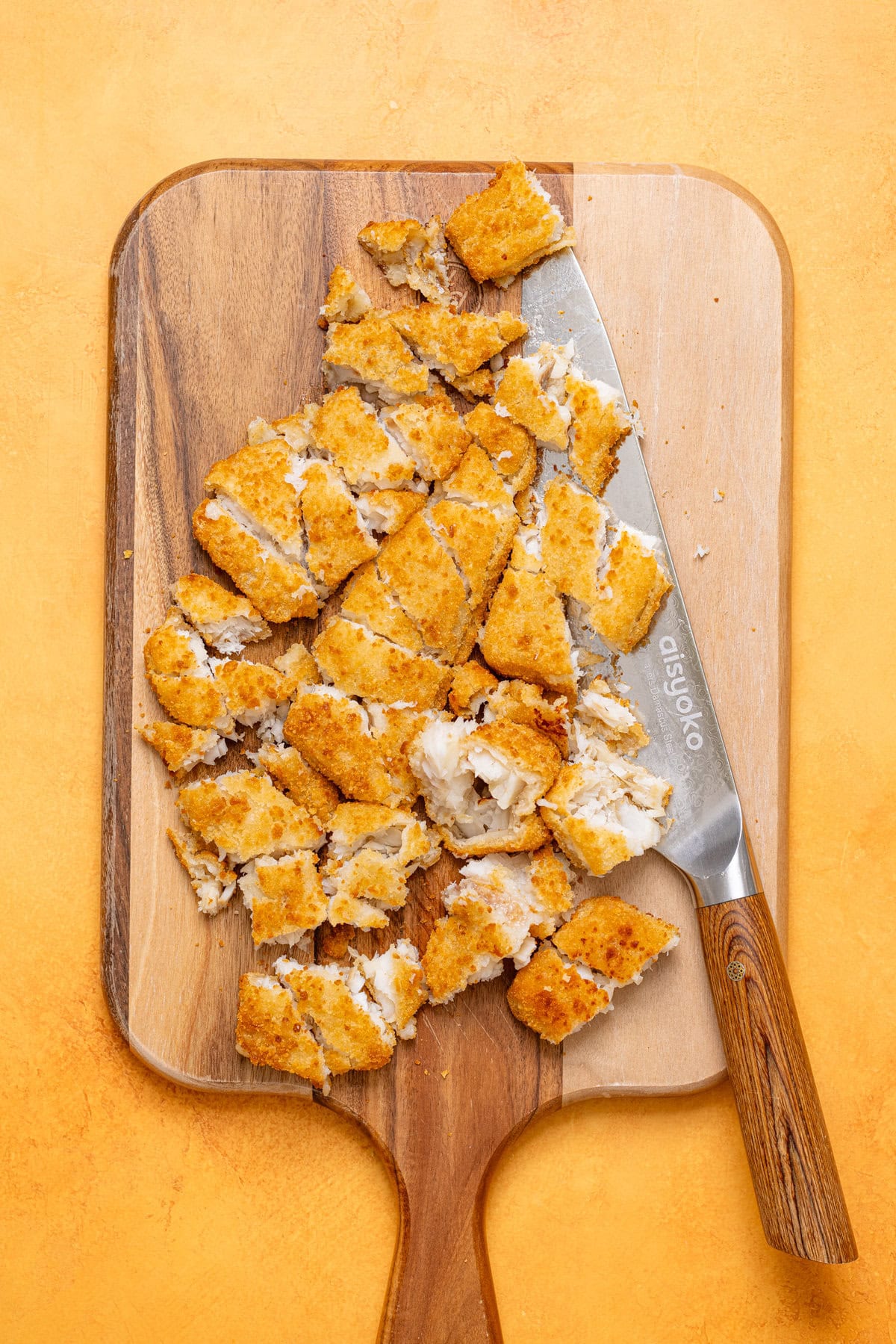 Chopped fish fillets on a cutting board with a knife.