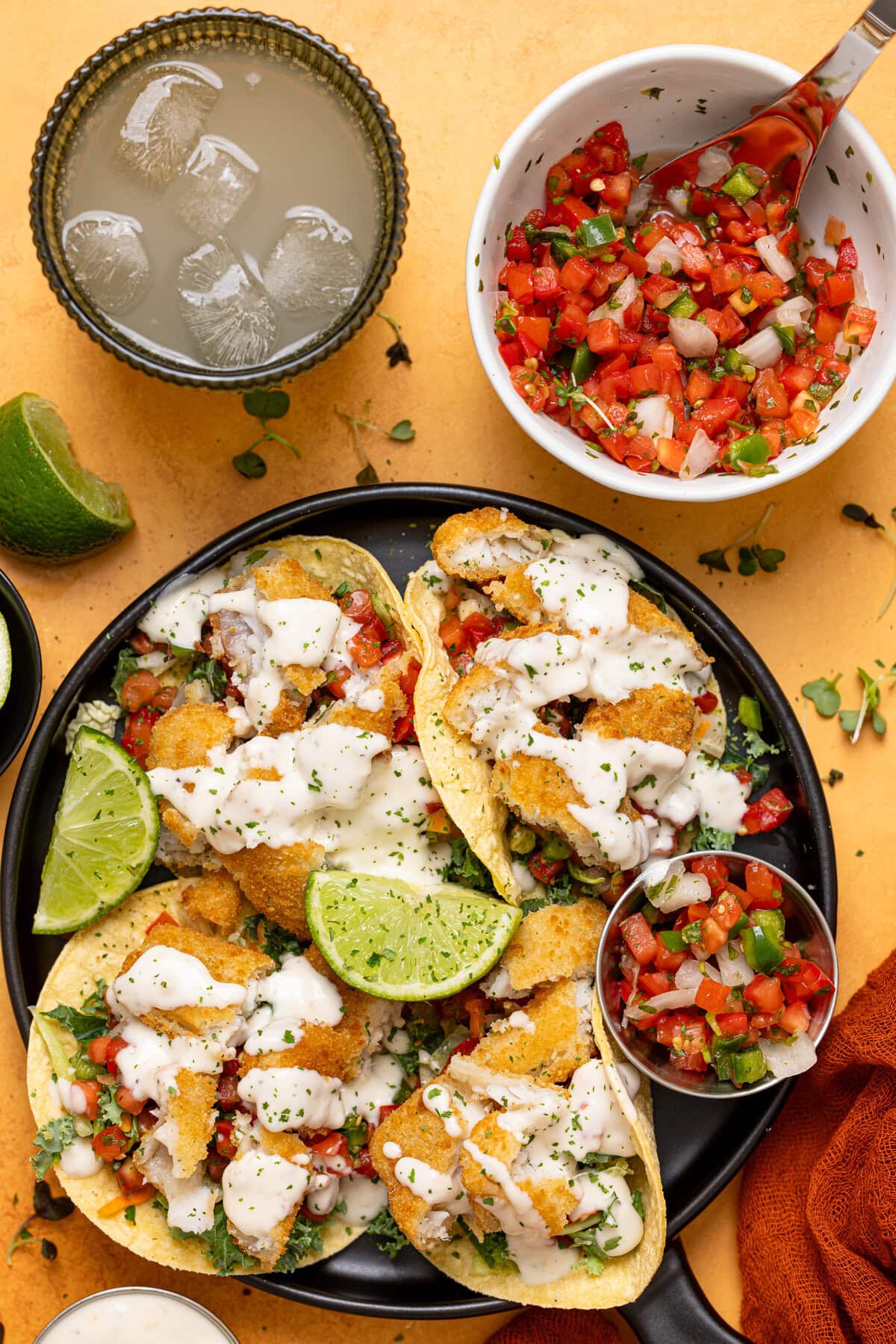 Tacos on a platter with a bowl of pice de gallo and drink.