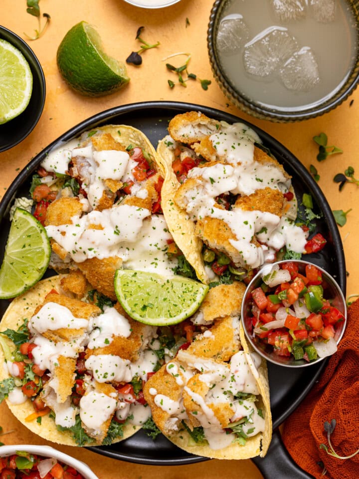 Fish tacos on a platter with lime and a drink.