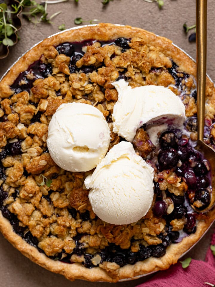 Blueberry crumble pie with scoops of vanilla ice cream and a spoon.