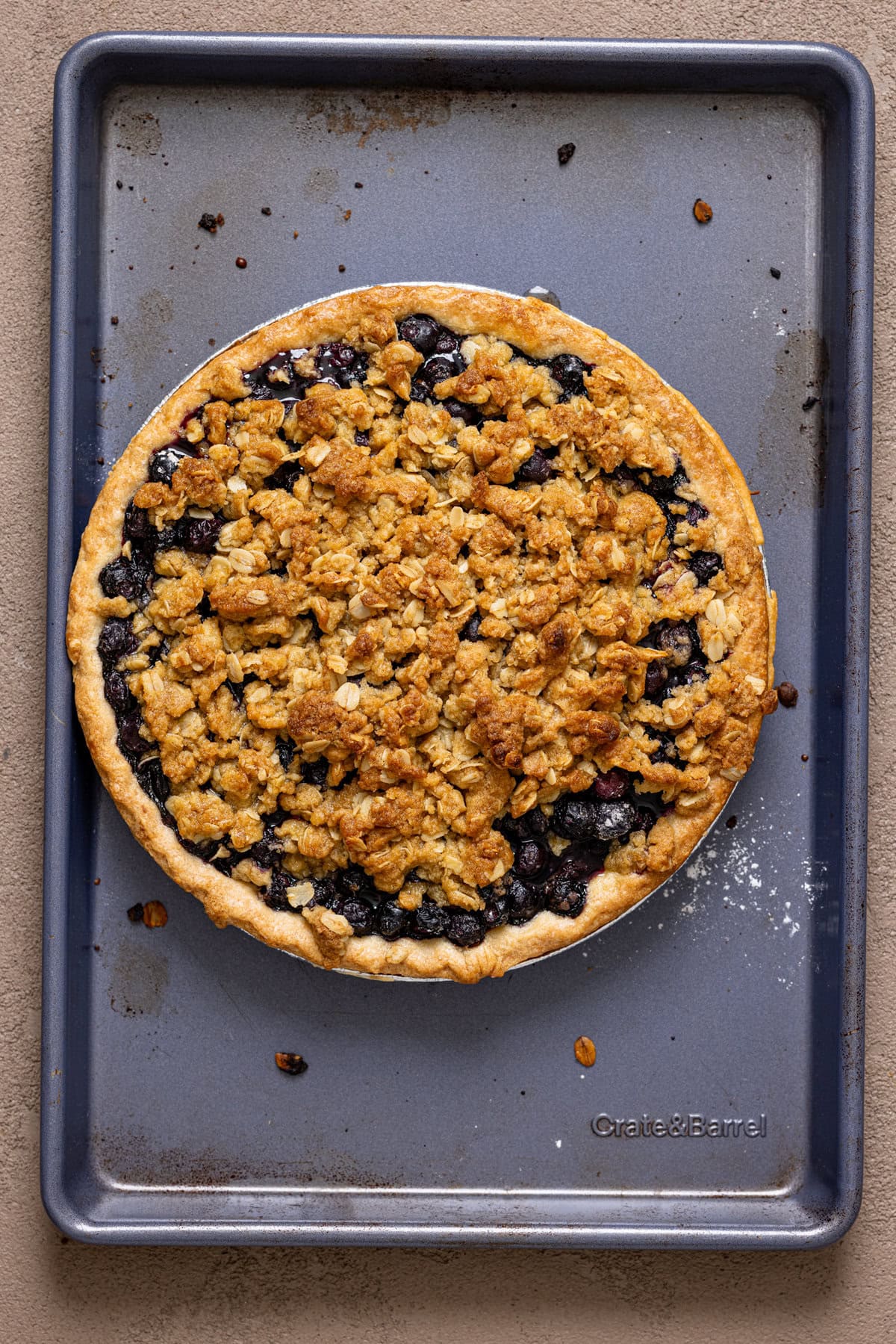 Baked blueberry crumble pie on a blue baking sheet.