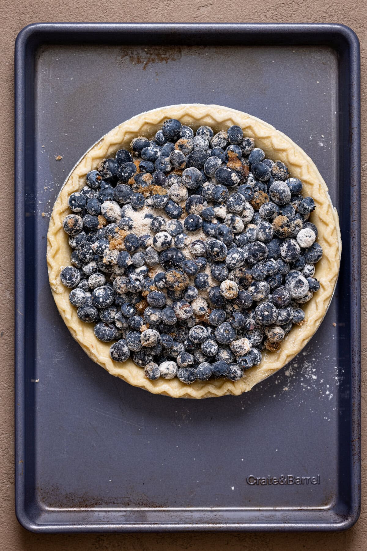 Blueberry crumble pie ingredients filled in a pie crust on a blue baking sheet.