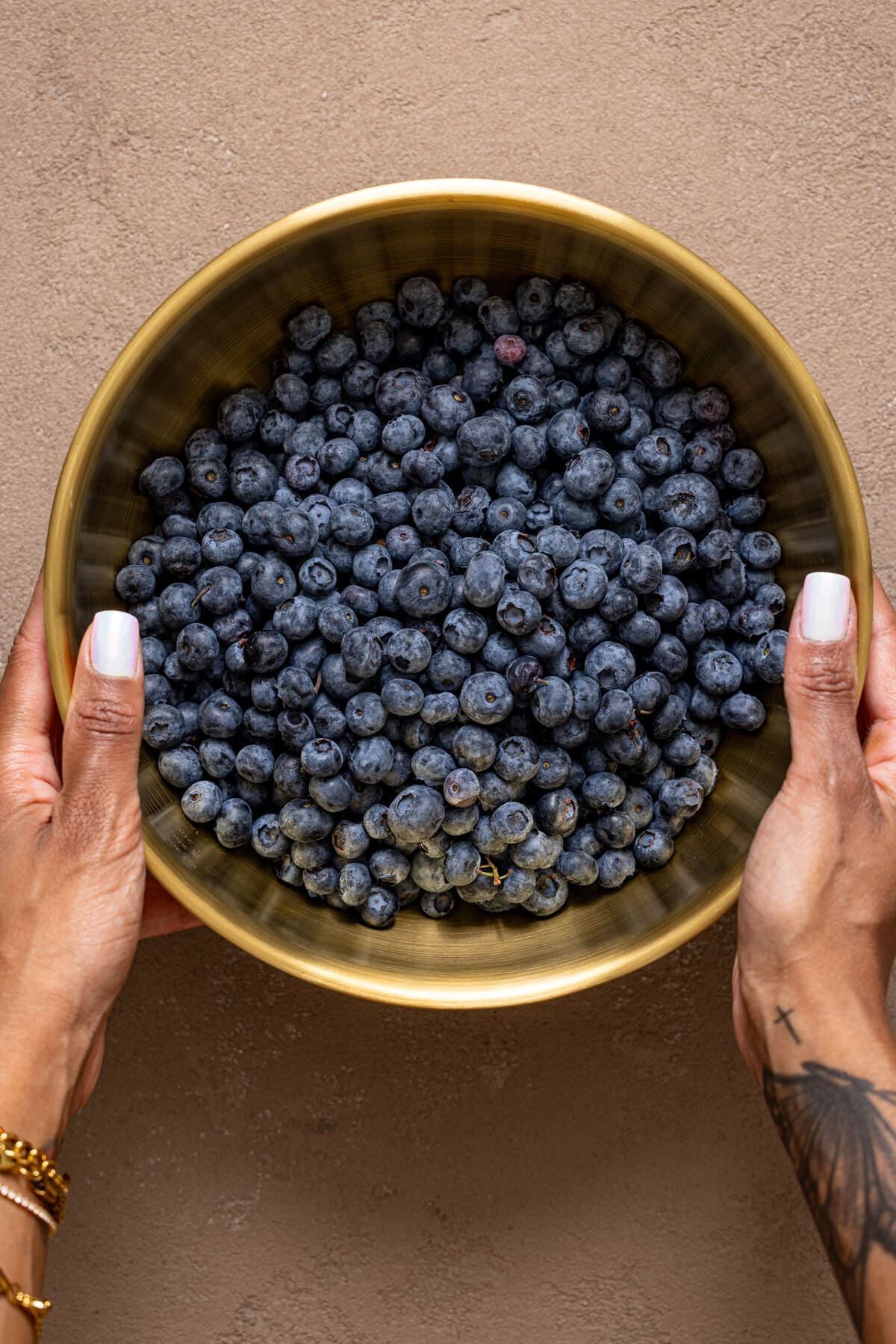 Gold bowl being held with hands and filled with blueberries.