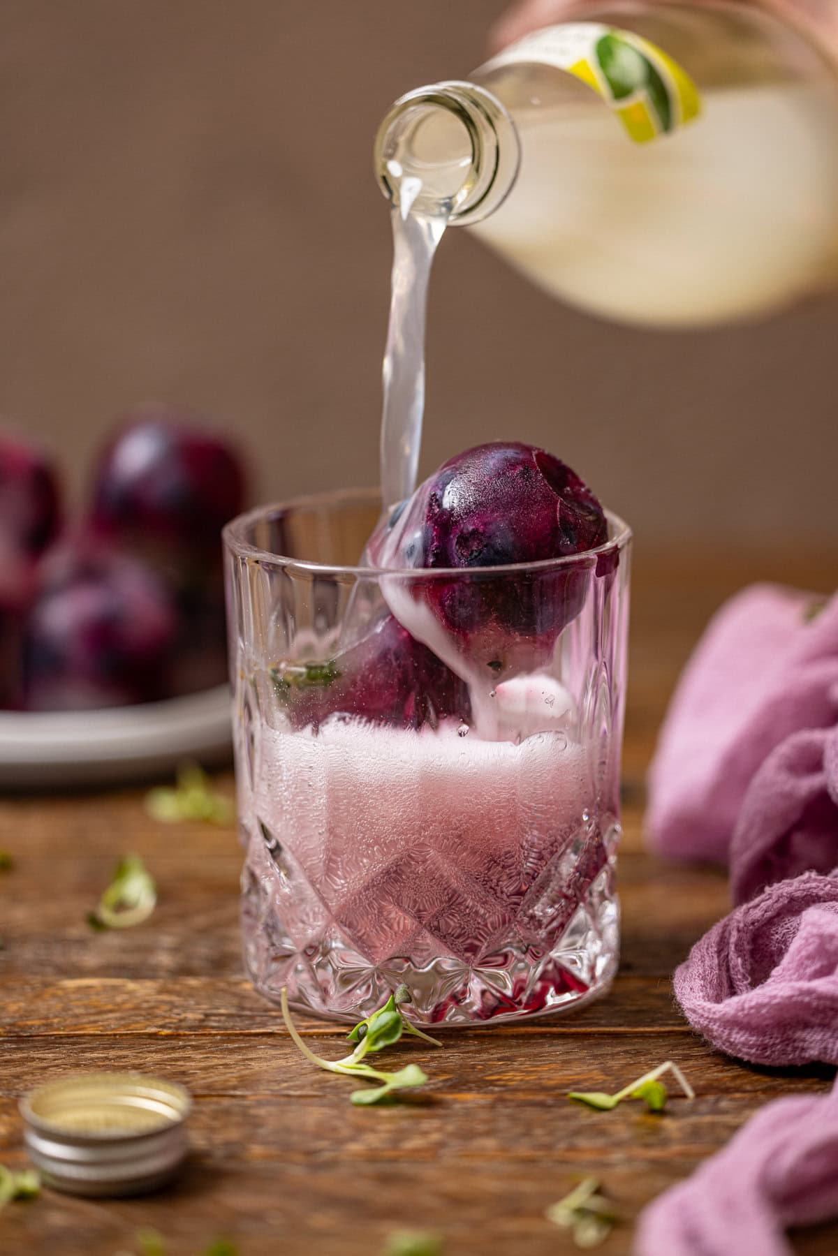 Blueberry ice cubes in a glass with lemon soda being poured.