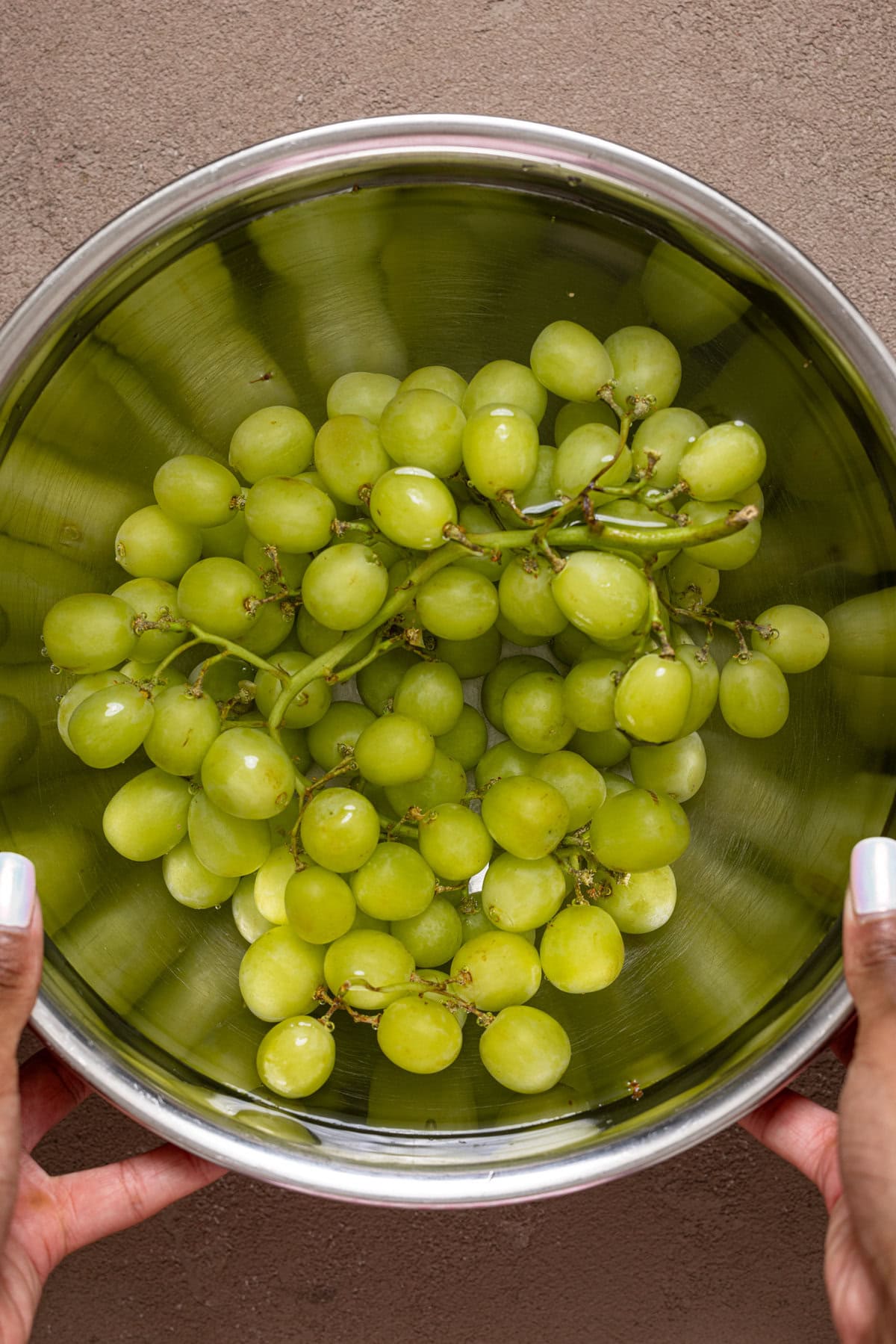 Fresh green grapes being held in a silver bowl.