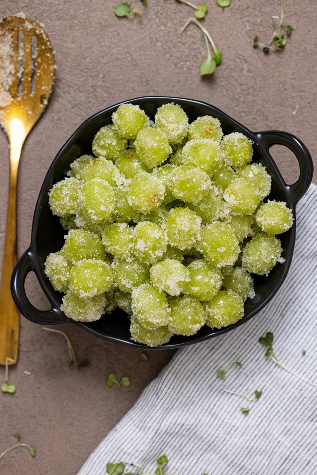 Candied grapes in a black bowl with a gold spoon.