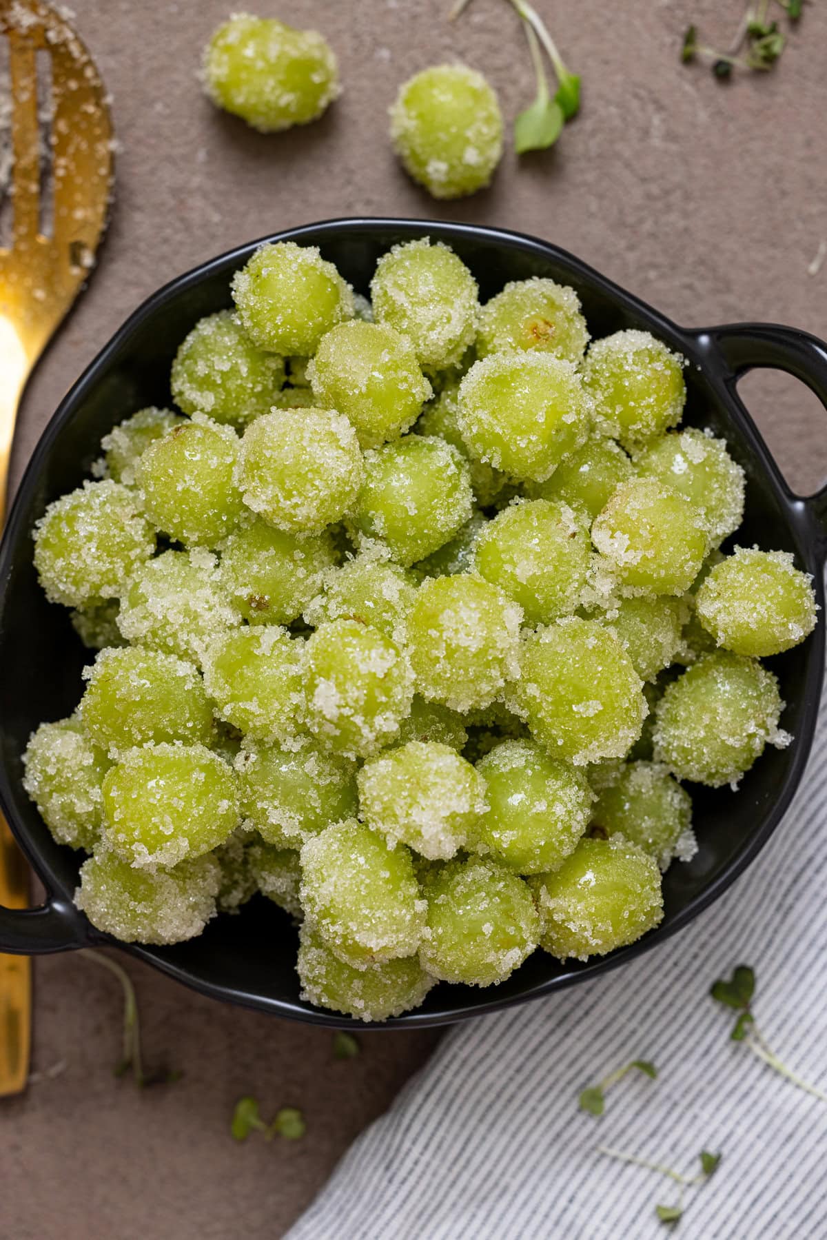 Coated candied grapes in a black bowl.