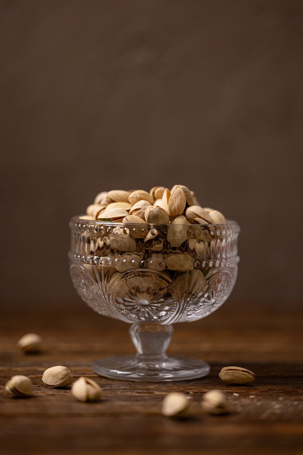 Pistachio nuts in a bowl on a brown wood table.