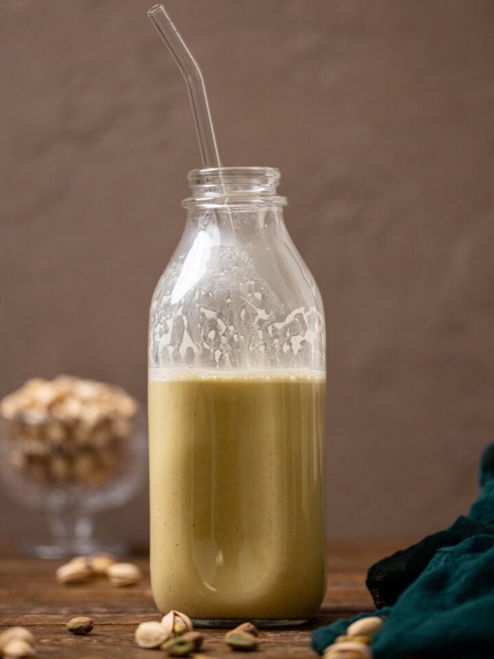 Pistachio milk in a glass bottle with a straw with nuts.