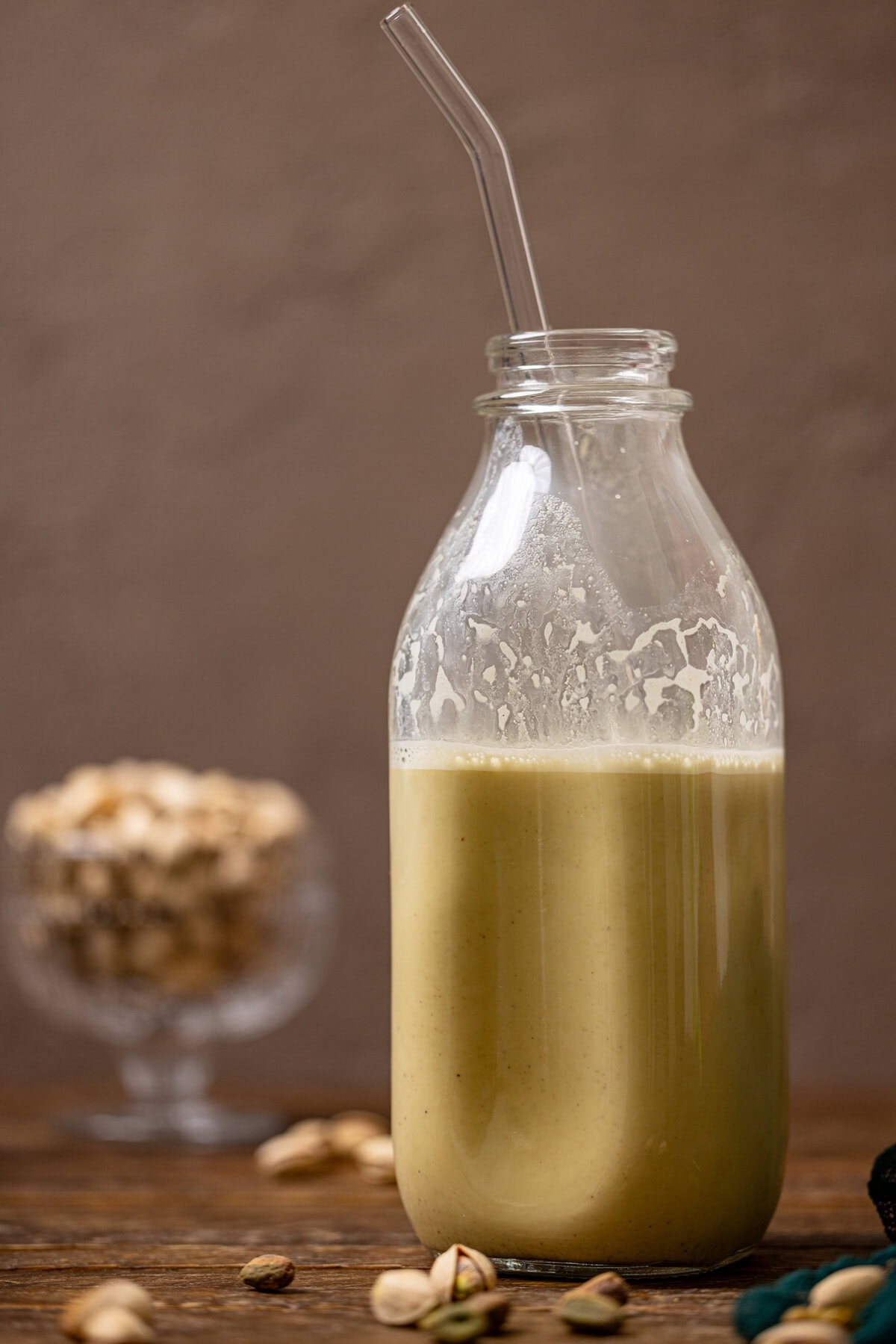 Pistachio milk in a glass bottle with a straw.