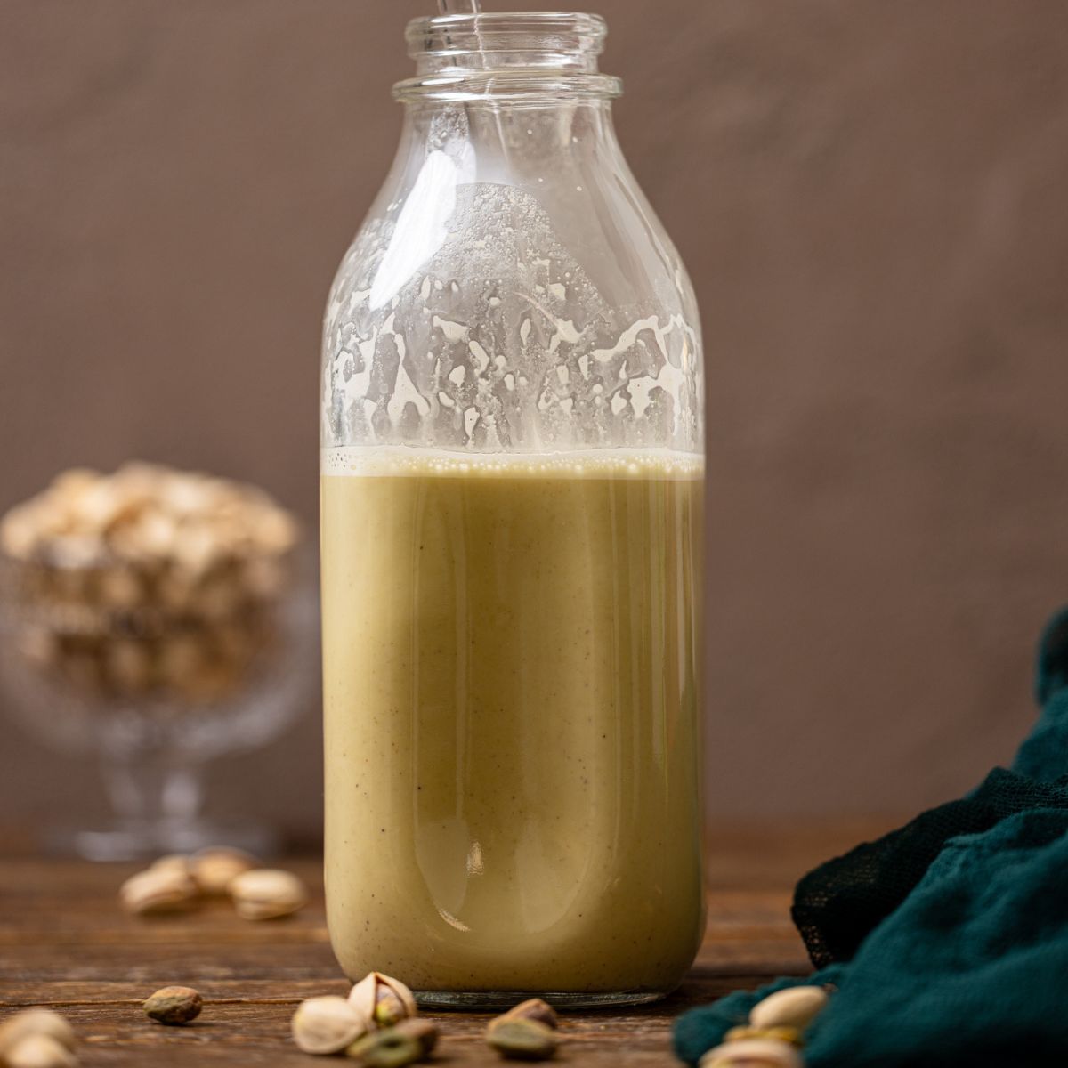 Pistachio milk in a glass bottle with a straw.