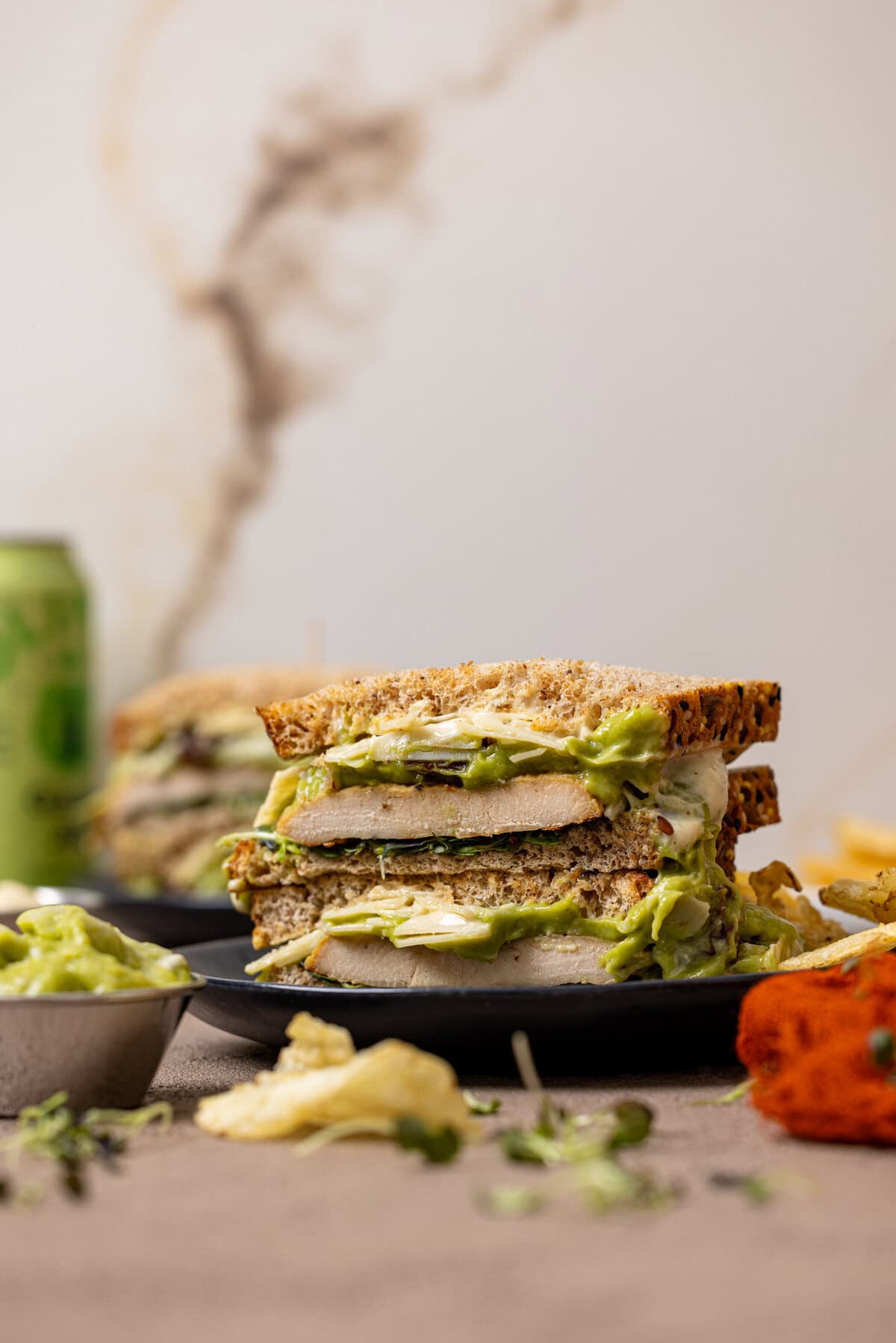 Two chicken avocado sandwiches on a plate with a drink in the background.