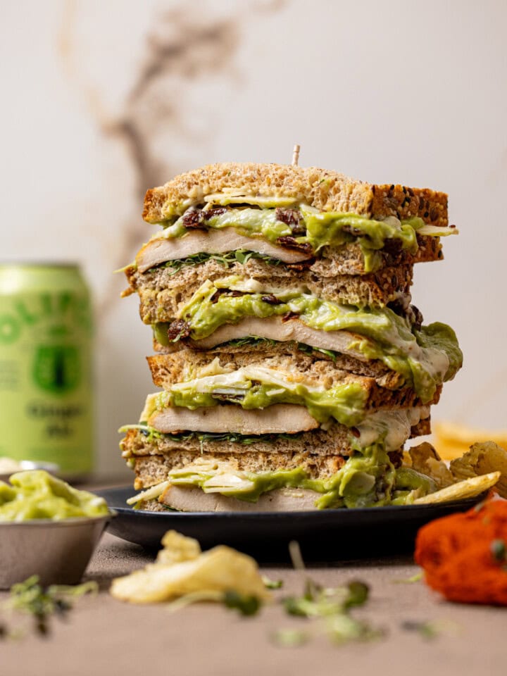 Chicken avocado sandwiches stacked on a plate with a drink and chips.