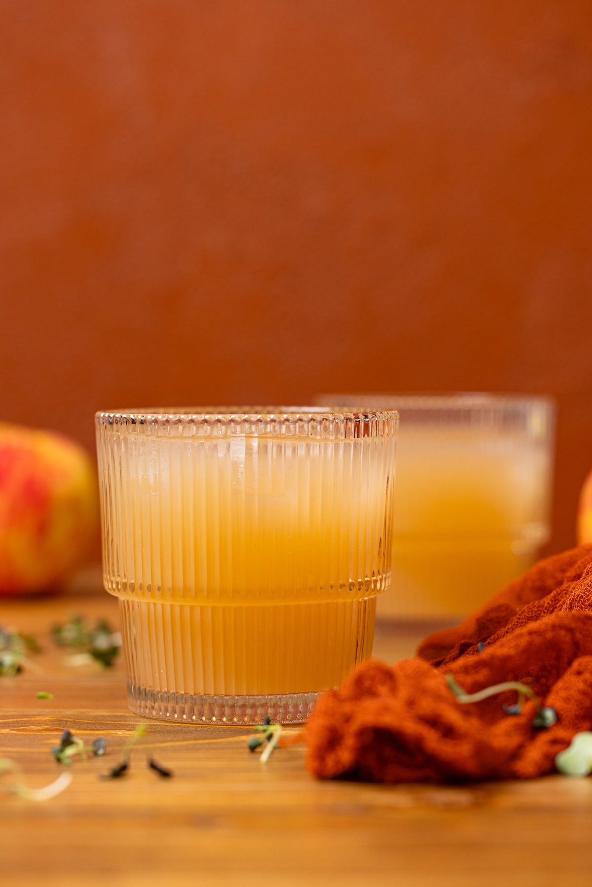 Two glasses of apple juice with an apple and red napkin.