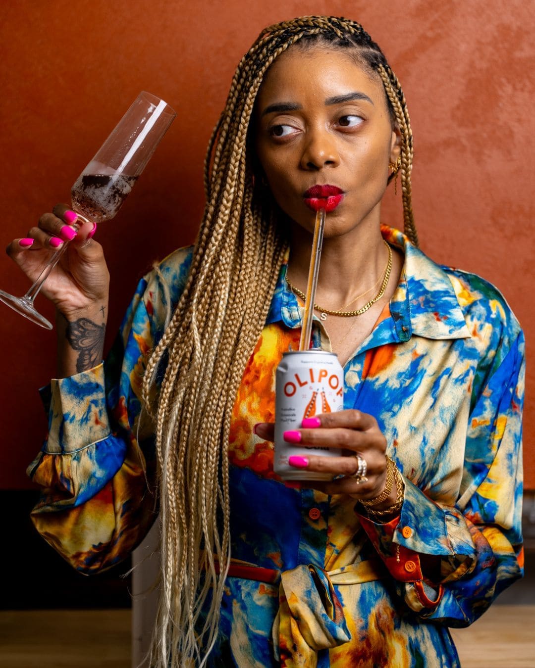 Shanika drinking out of a can with a straw and holding a wine glass.