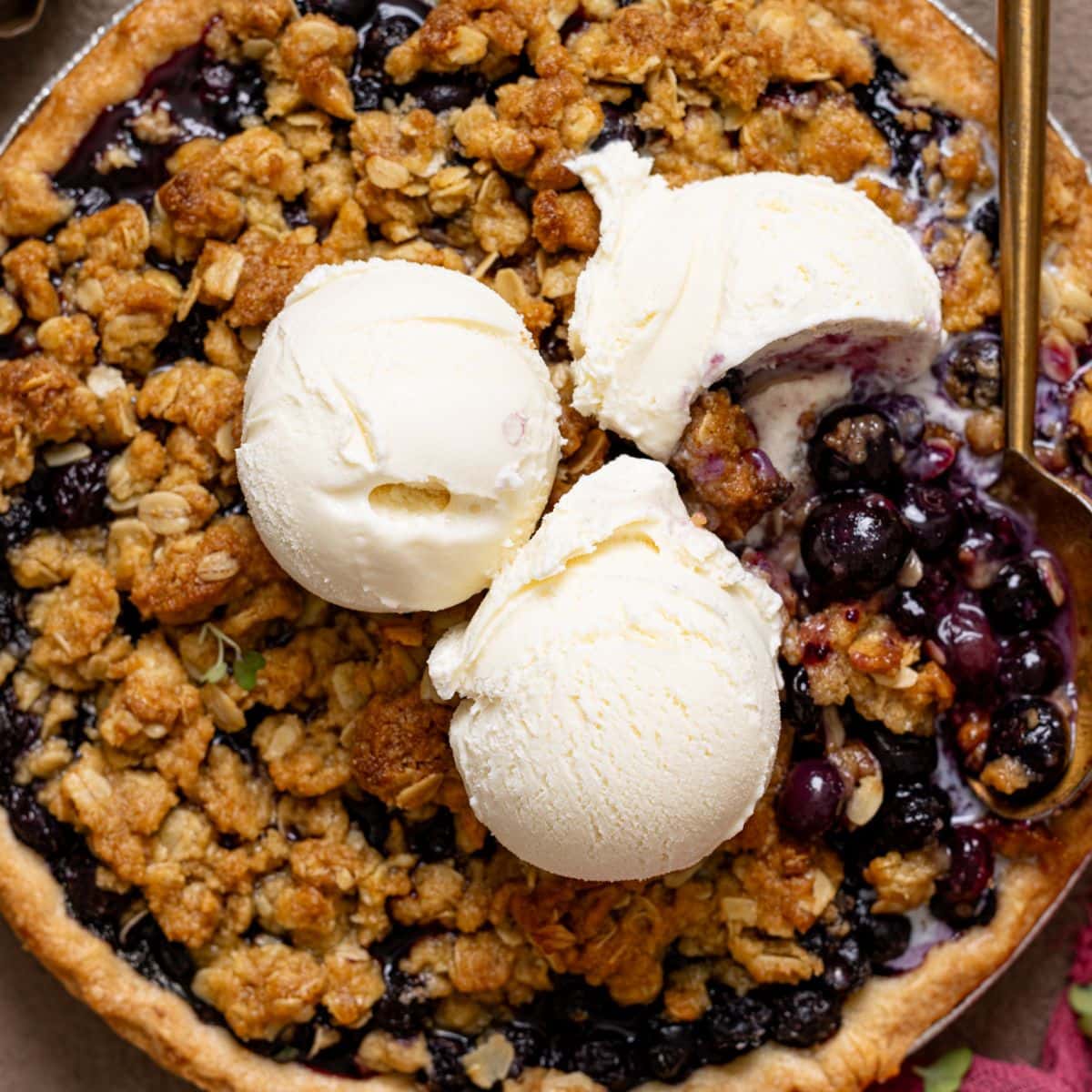 Blueberry crumble pie with scoops of vanilla ice cream and a spoon.