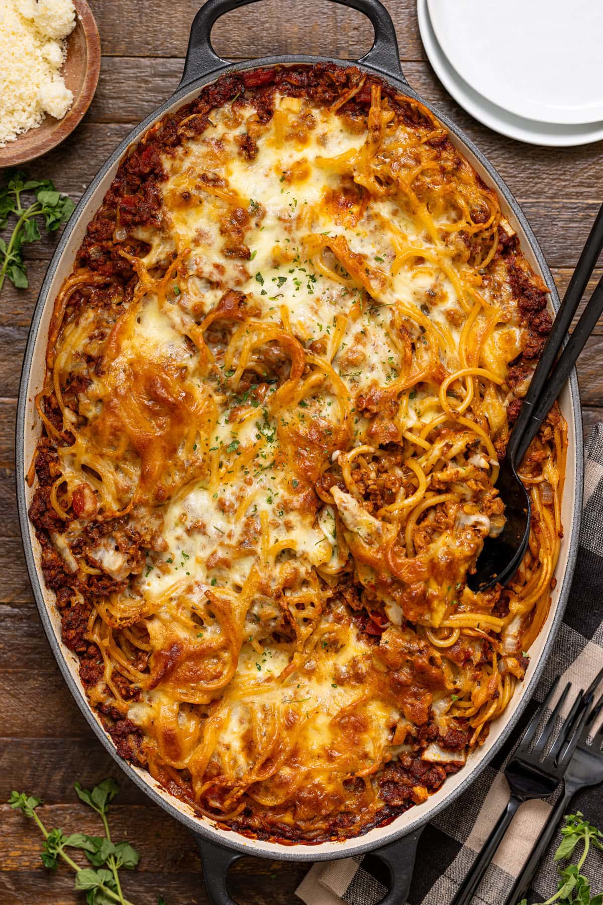 Baked spaghetti in a baking dish with a spoon and white plates.