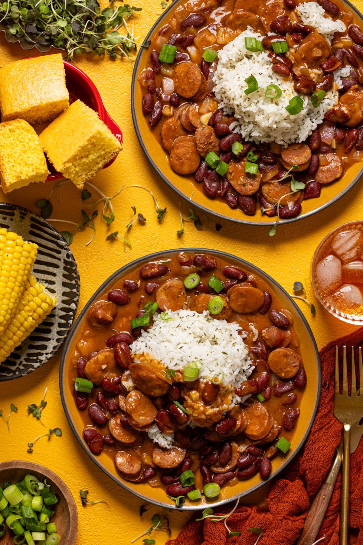 Red beans and rice in two plates on a yellow table with cornbread and a drink.