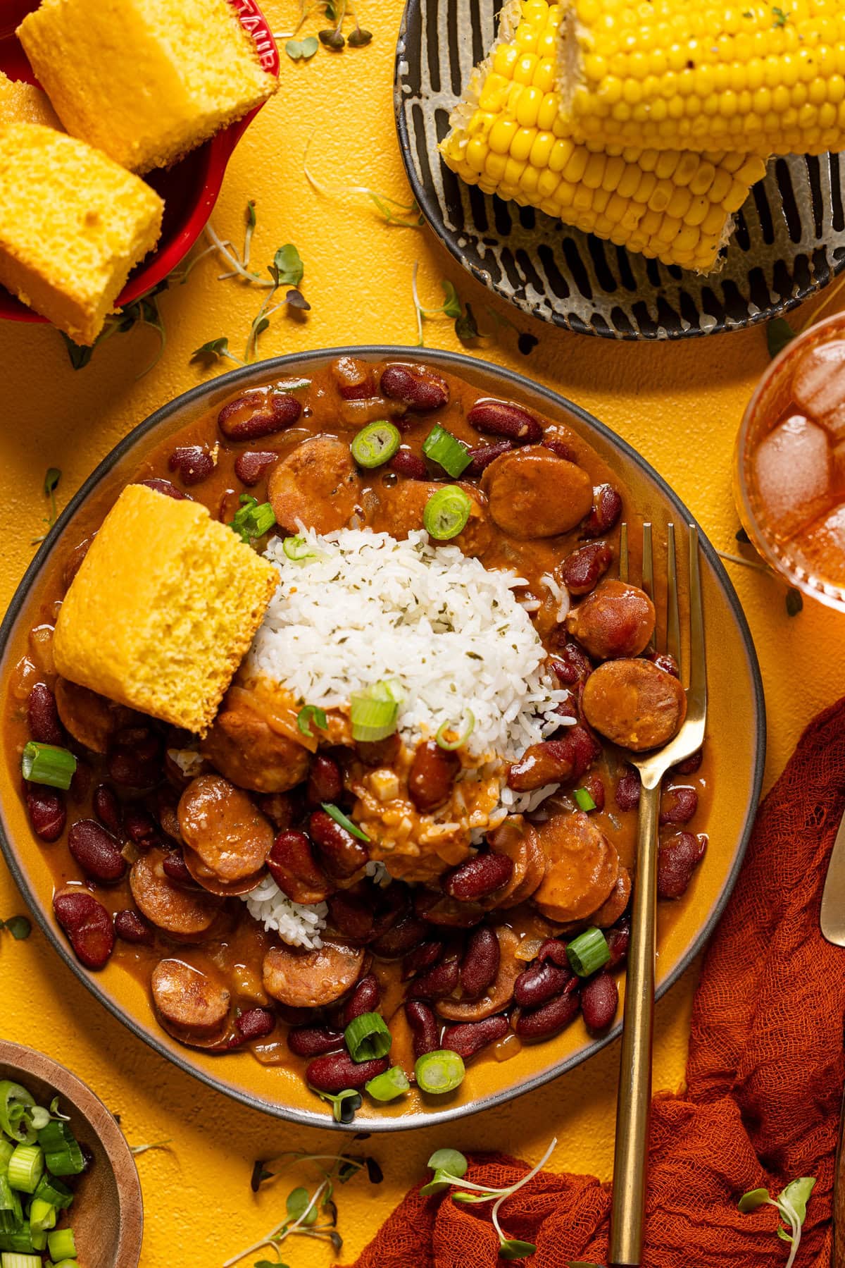 Up close shot of plate with red beans and rice, cornbread, a drink, and a fork. 