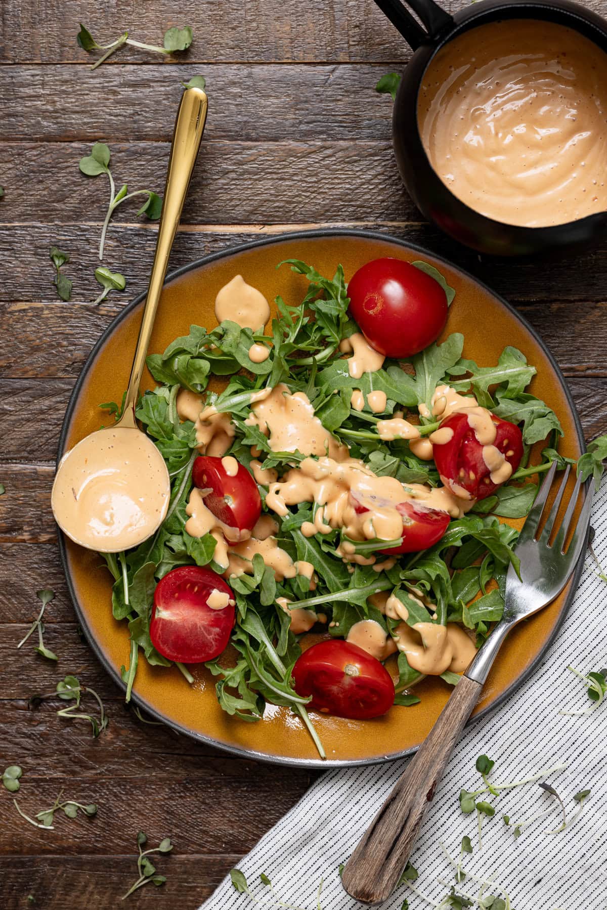 Plate with salad with thousand island dressing atop with a spoon and fork.