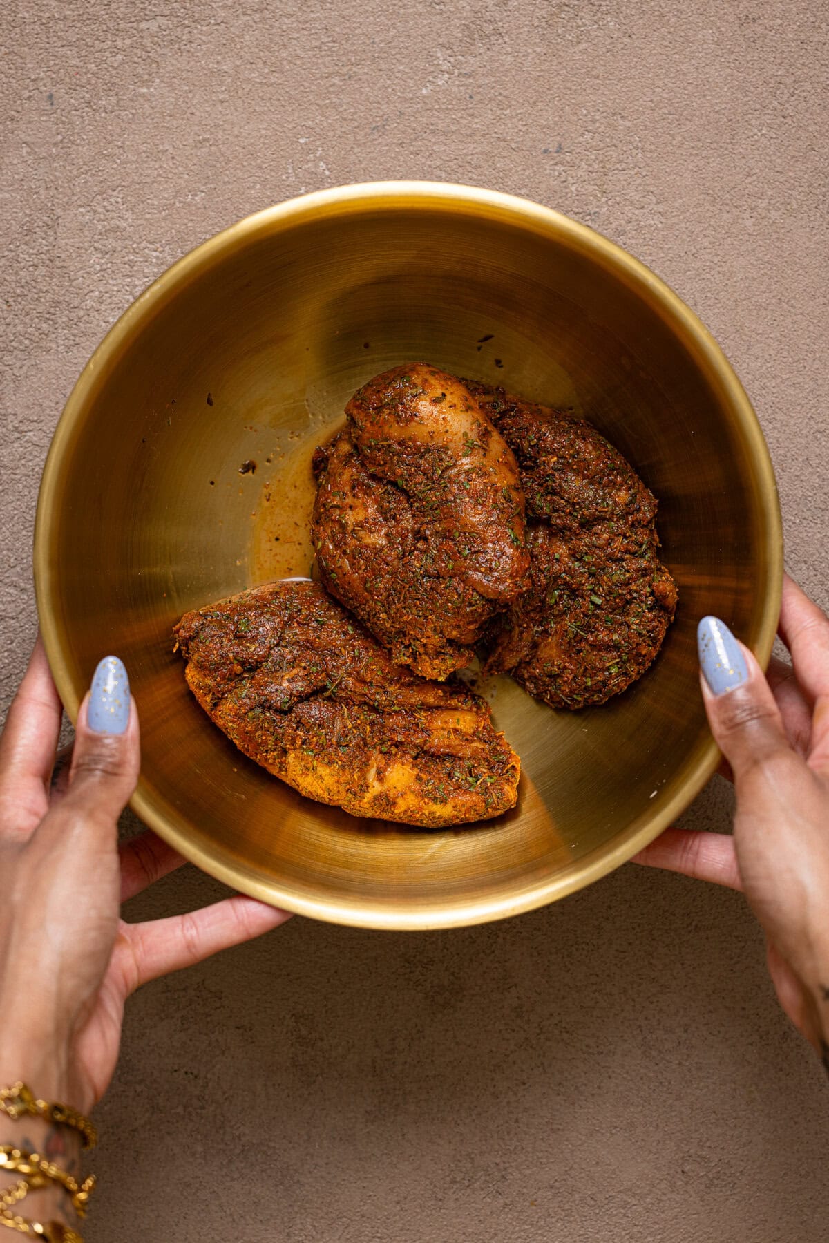 Seasoned chicken in a gold bowl being held with hands.