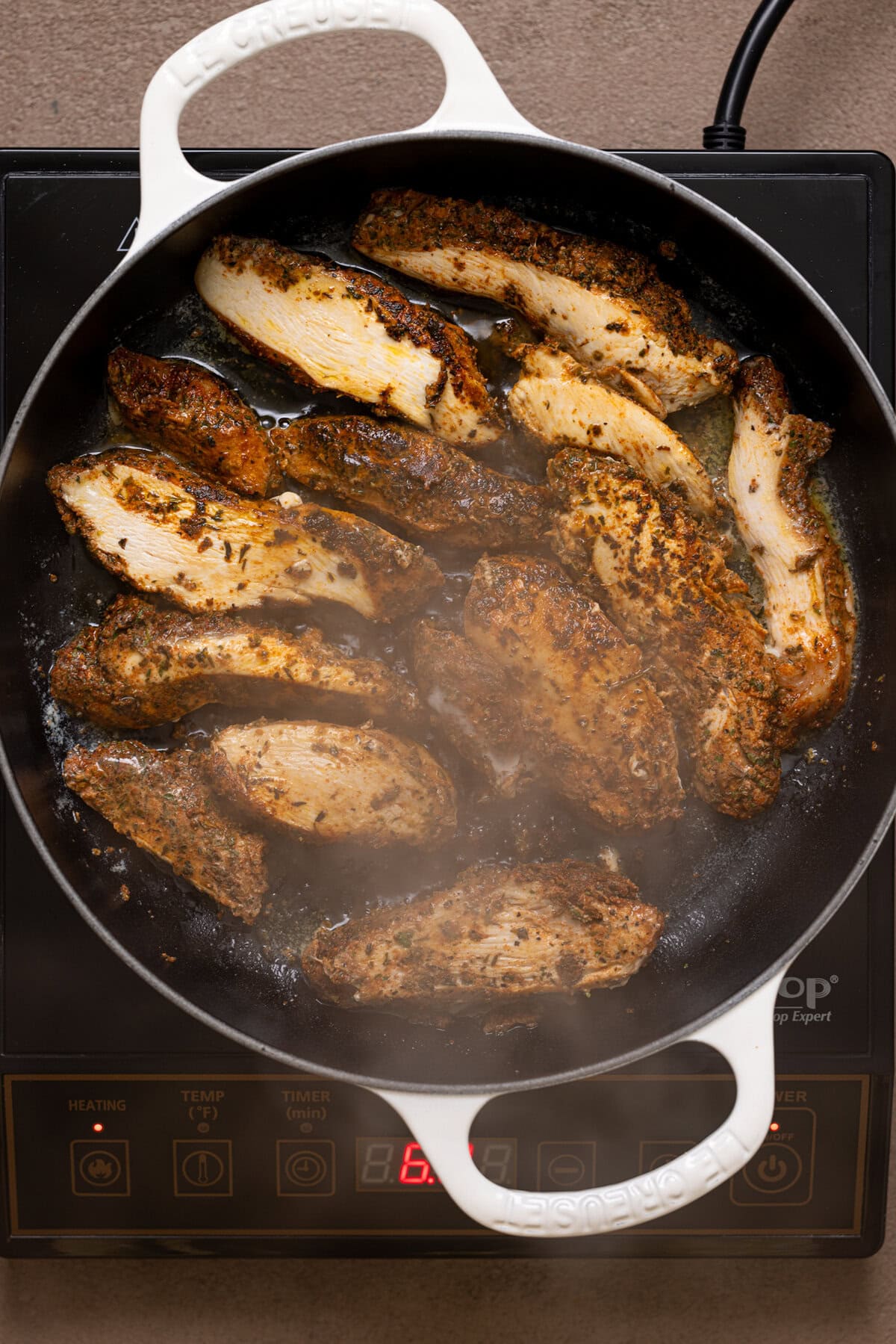 Chicken being seared in a white pan over the stovetop.