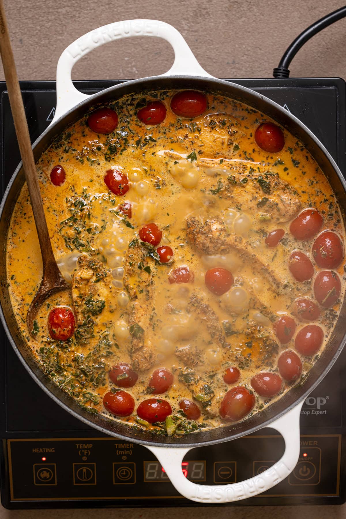 Tuscan sauce ingredients in a white pot over the stovetop.