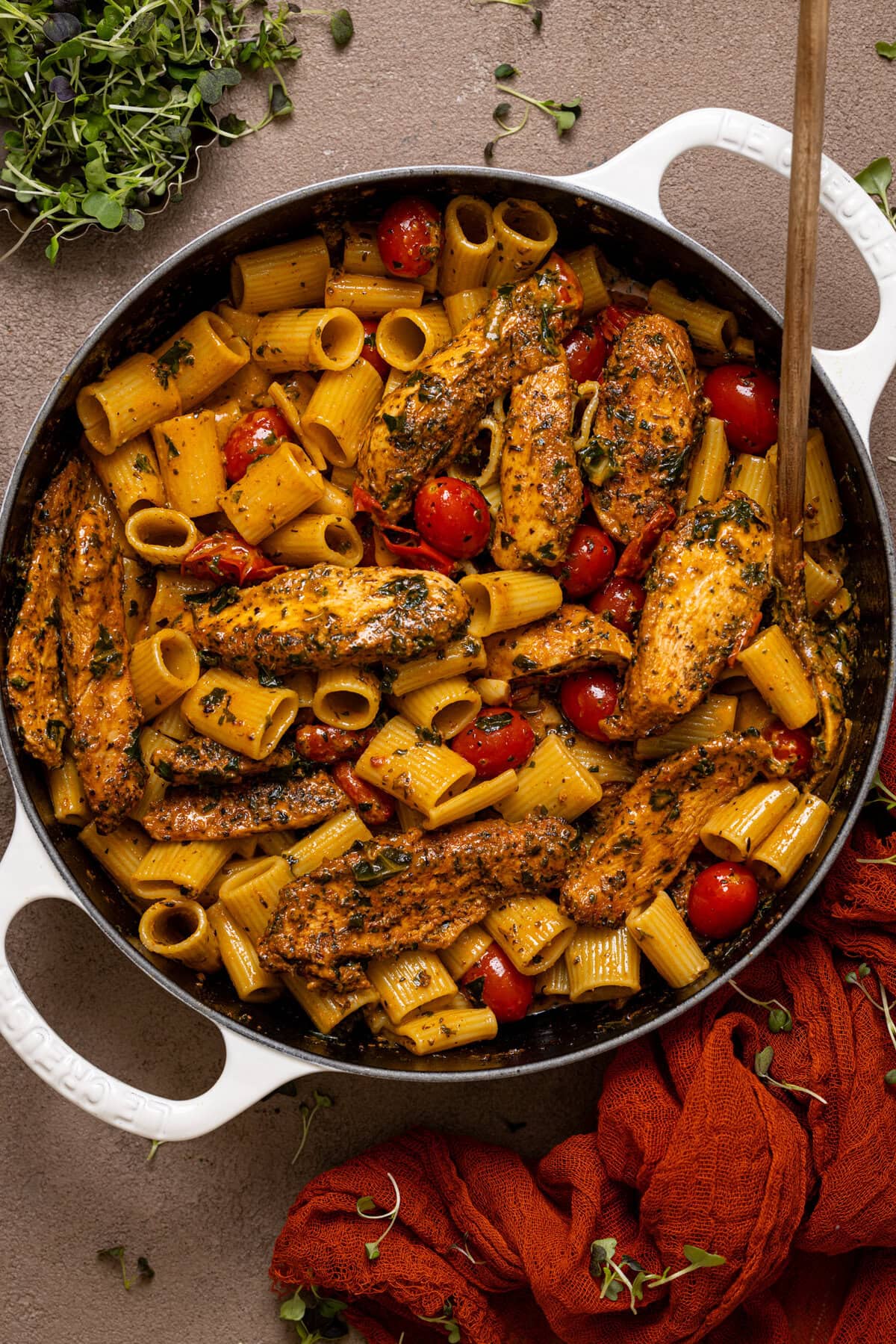 Cooked Tuscan Chicken pasta in a white pot with a spoon.