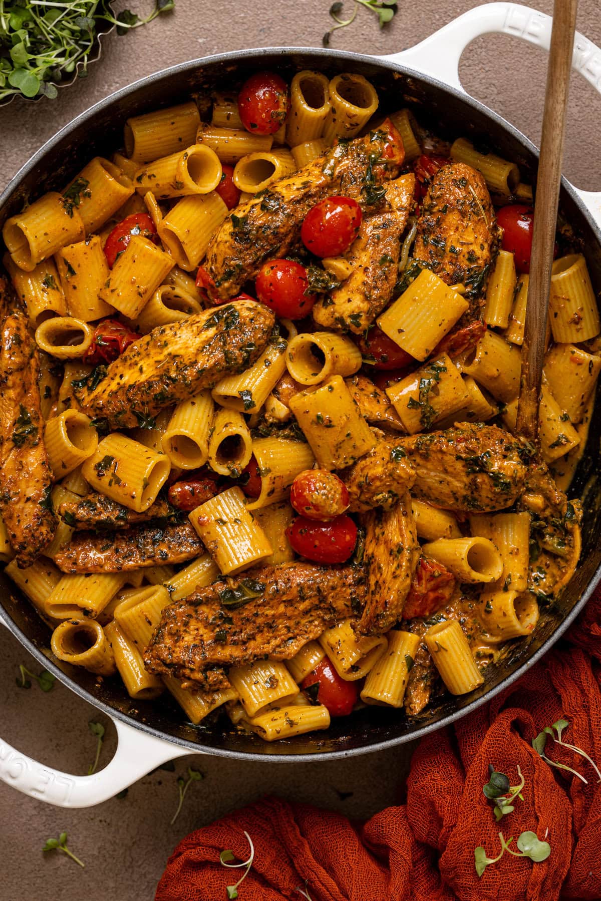 Tuscan Chicken pasta in a white pot on a grey-brownish table with a spoon.