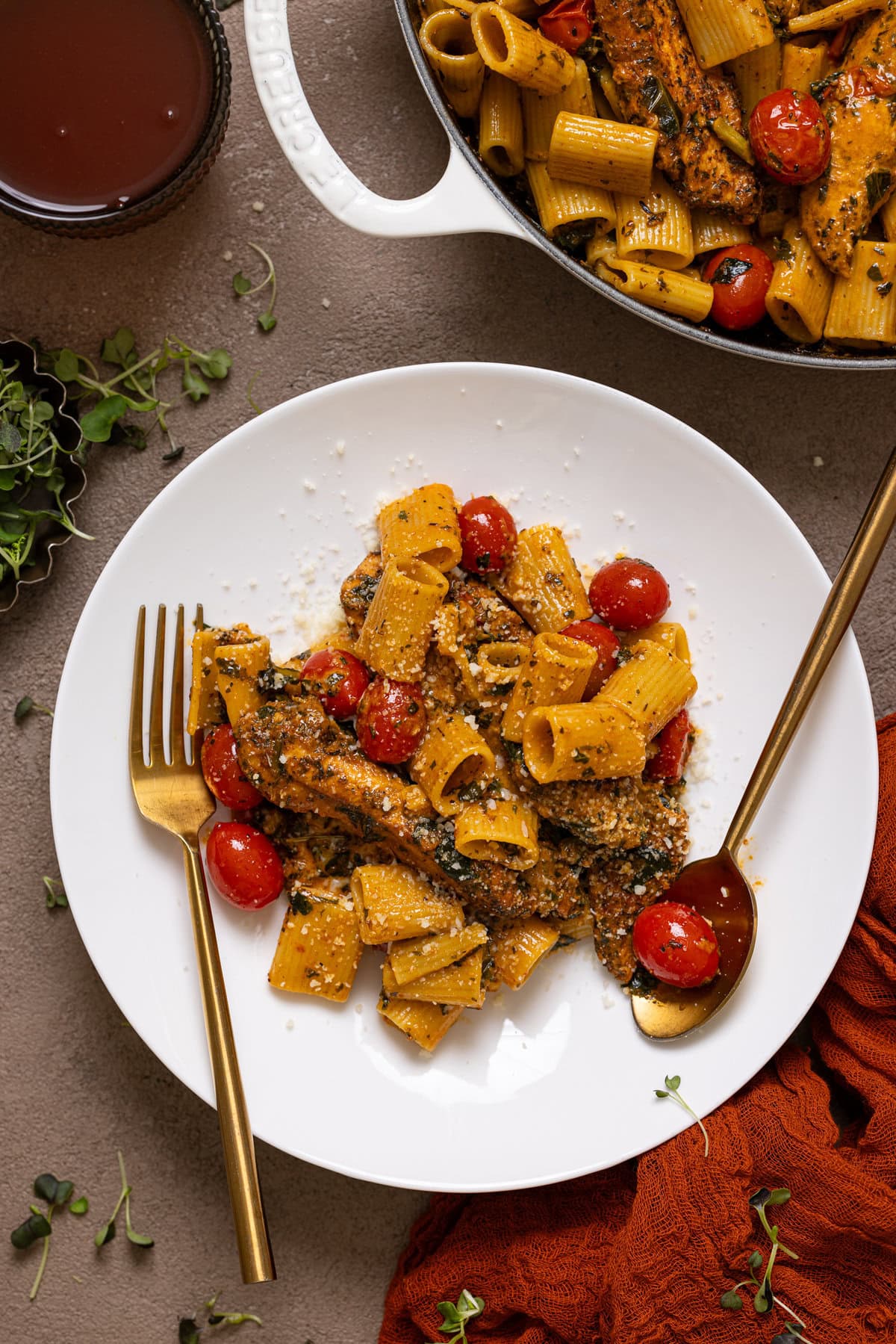 Tuscan chicken pasta on a white plate with a fork and drink.