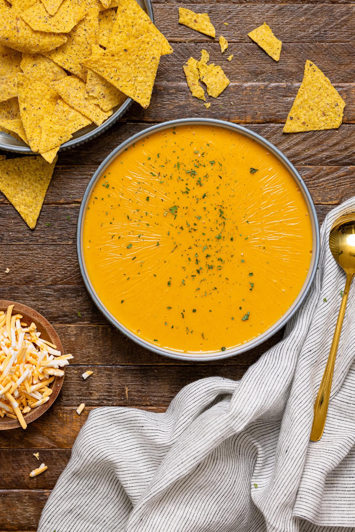 Bowl of nacho cheese with a spoon, cheese, and tortilla chips.