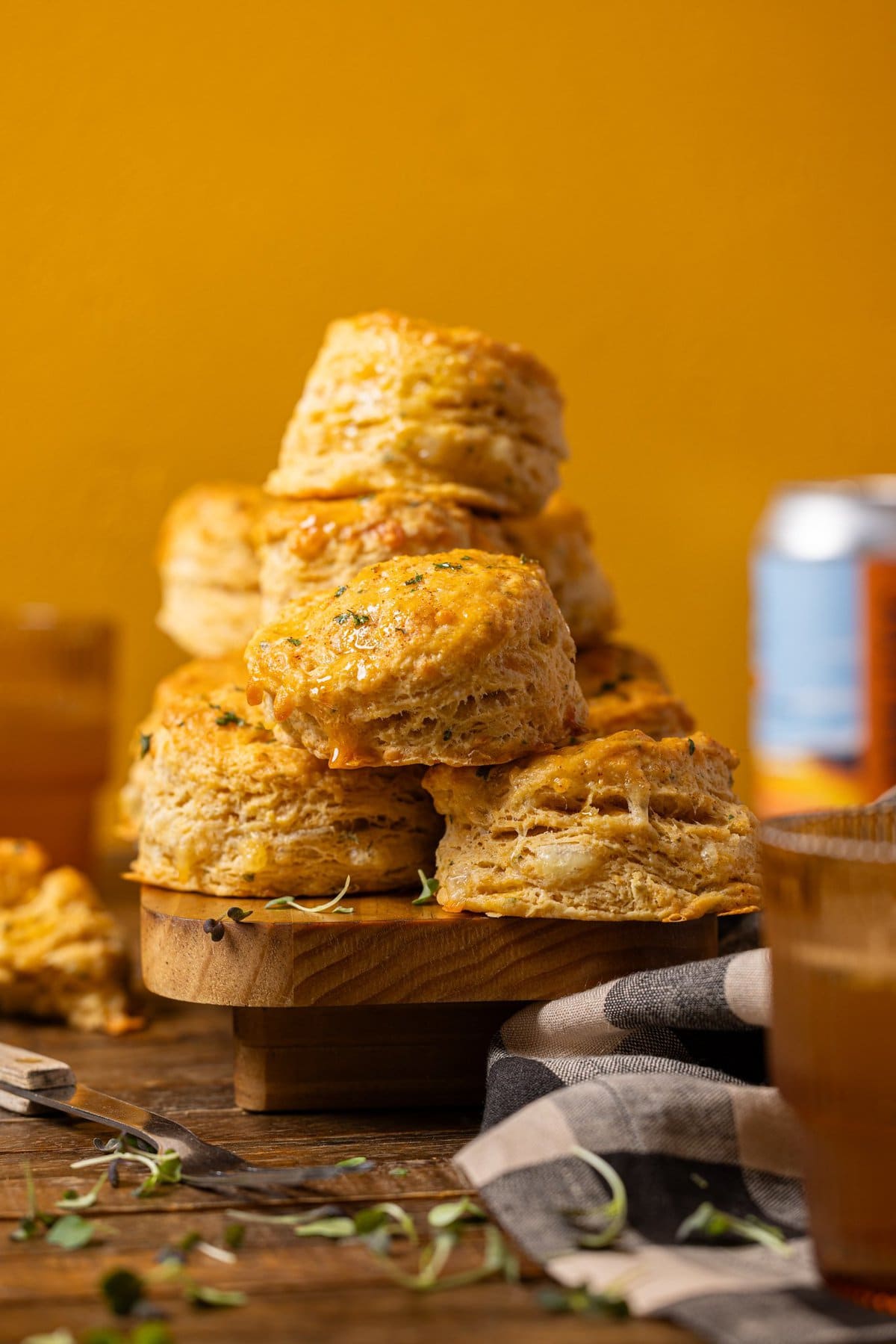 Stacked biscuits on a wood platter with a can and drinks in the background.