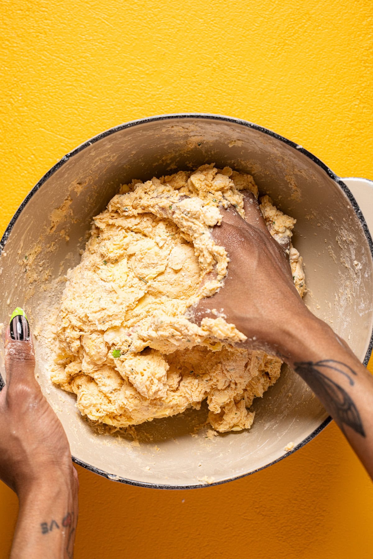 Biscuit dough in a bowl being kneaded with hand on a yellow table.