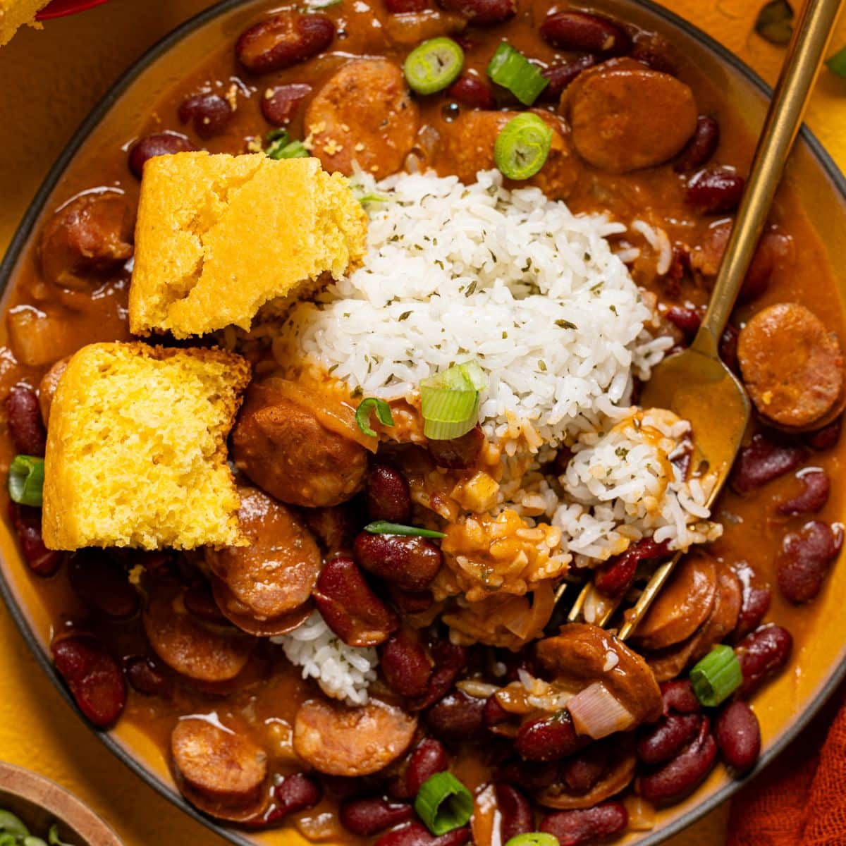 Up close shot of red beans and rice in a plate with a fork and cornbread.