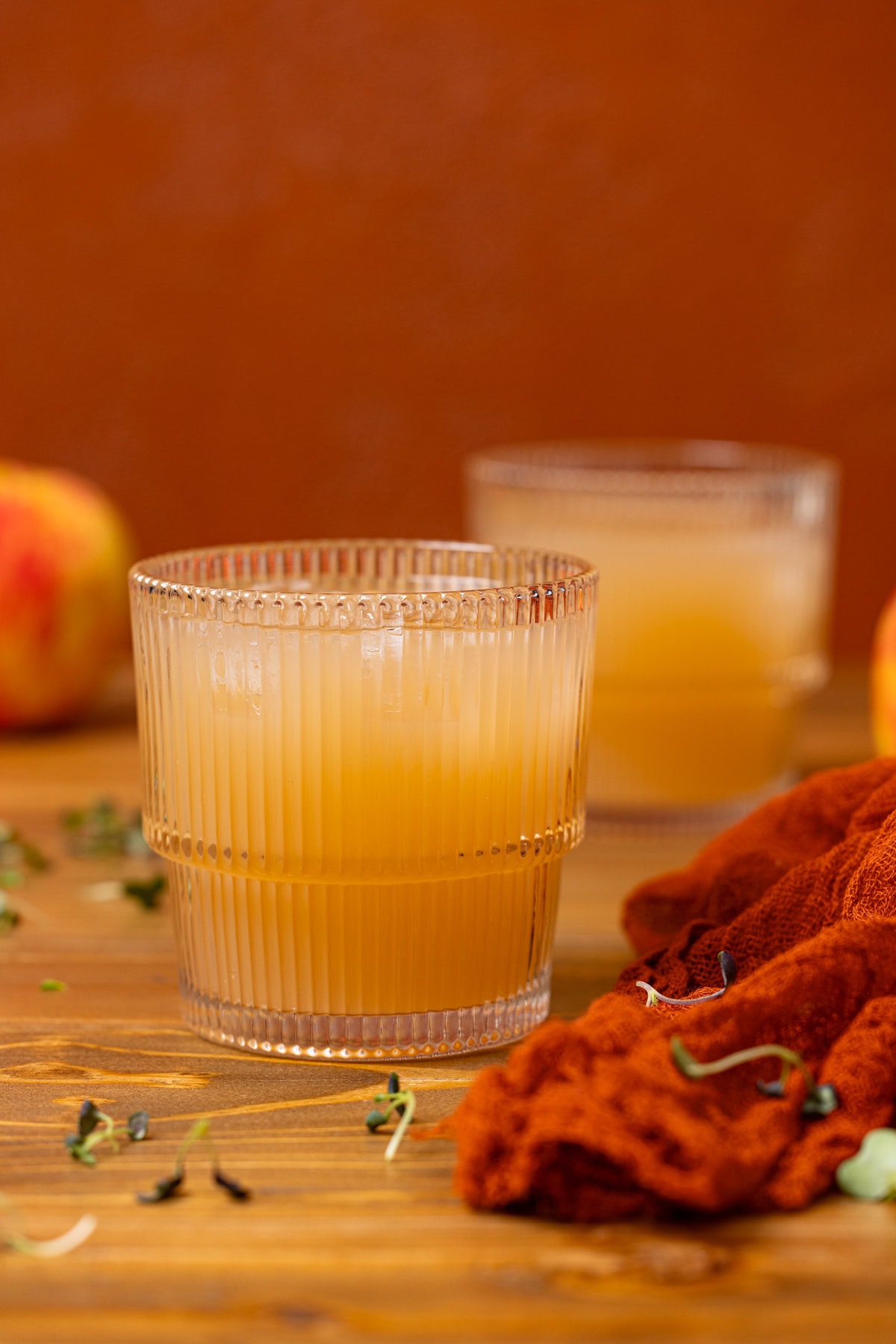 Two glasses of apple juice with apples.