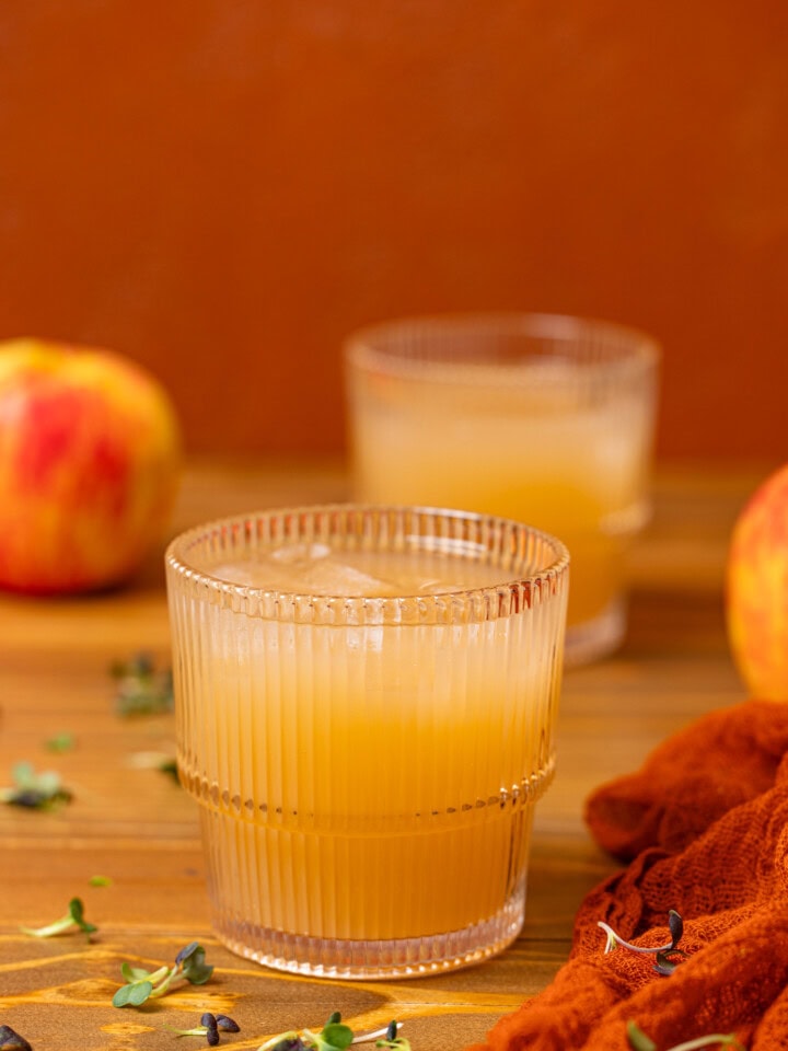 Two glasses of apple juice on a brown wood table with apples.