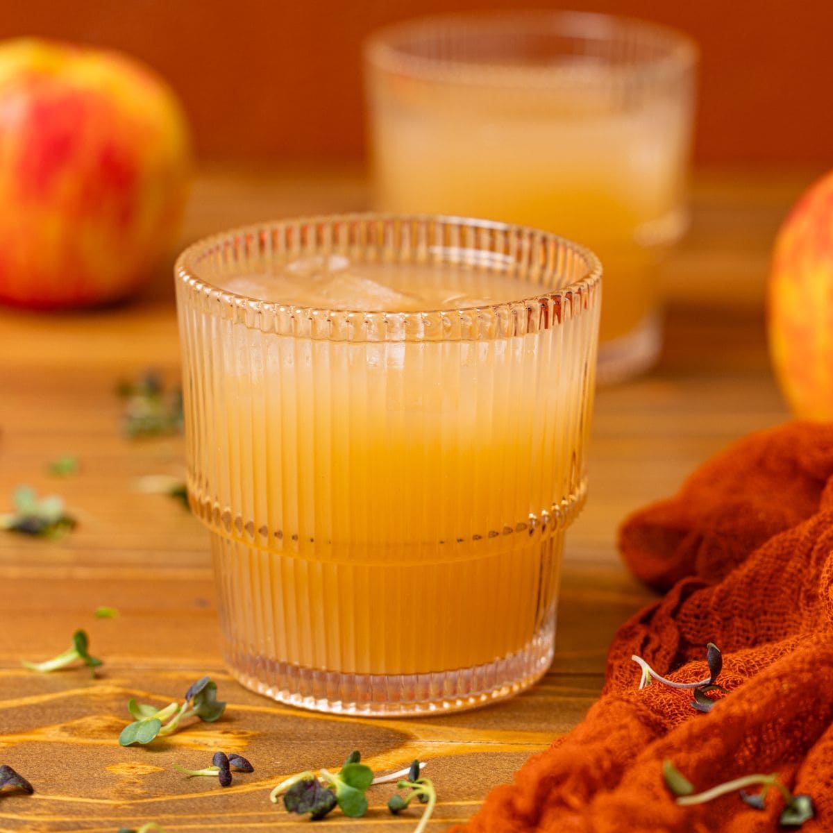 Two glasses of apple juice on a brown wood table with apples.