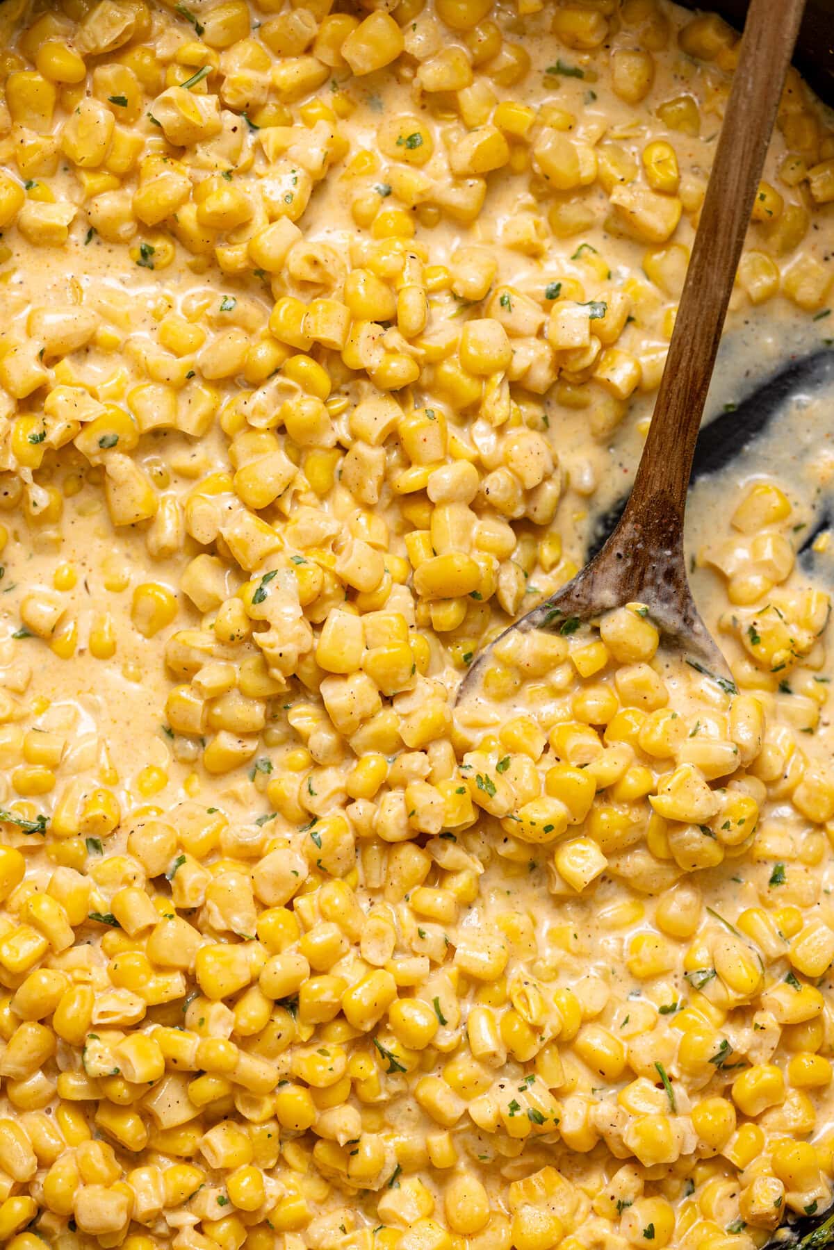 Up close shot of creamed corn with a wooden spoon.