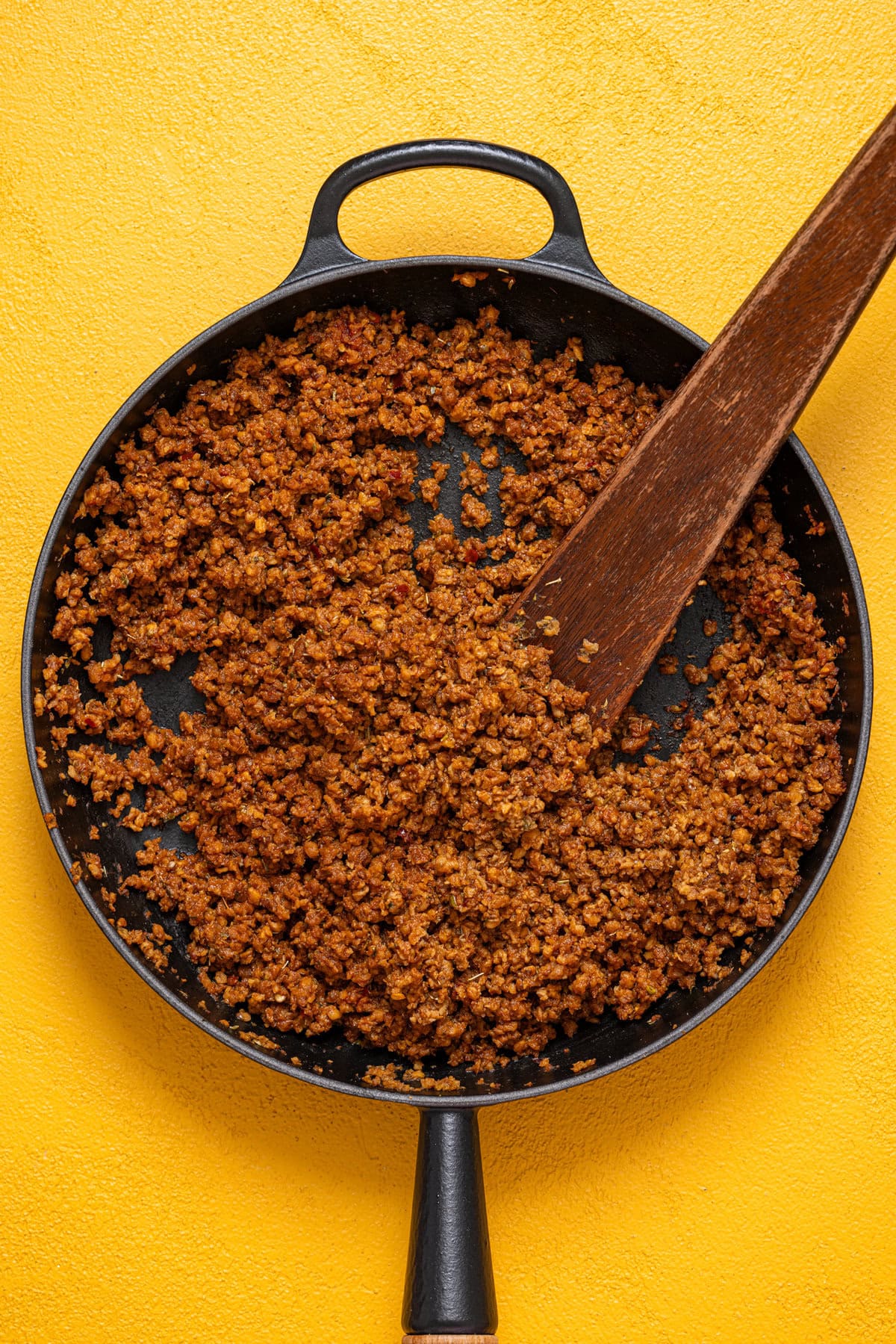 Plant-based taco meat cooked in a skillet with a wooden spoon.