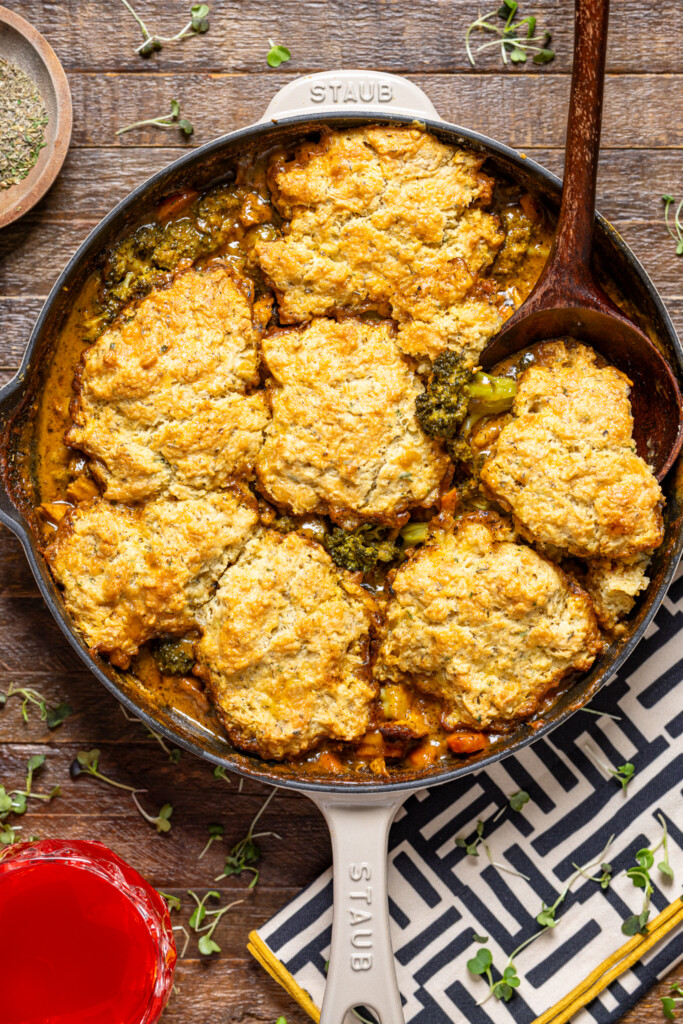 Broccoli cheddar pot pie in a skillet with a wooden spoon on a brown wood table.