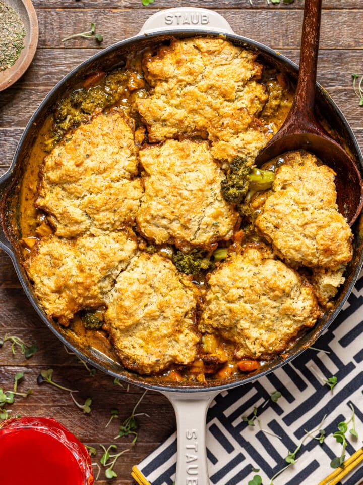 Broccoli cheddar pot pie in a skillet with a wooden spoon on a brown wood table.