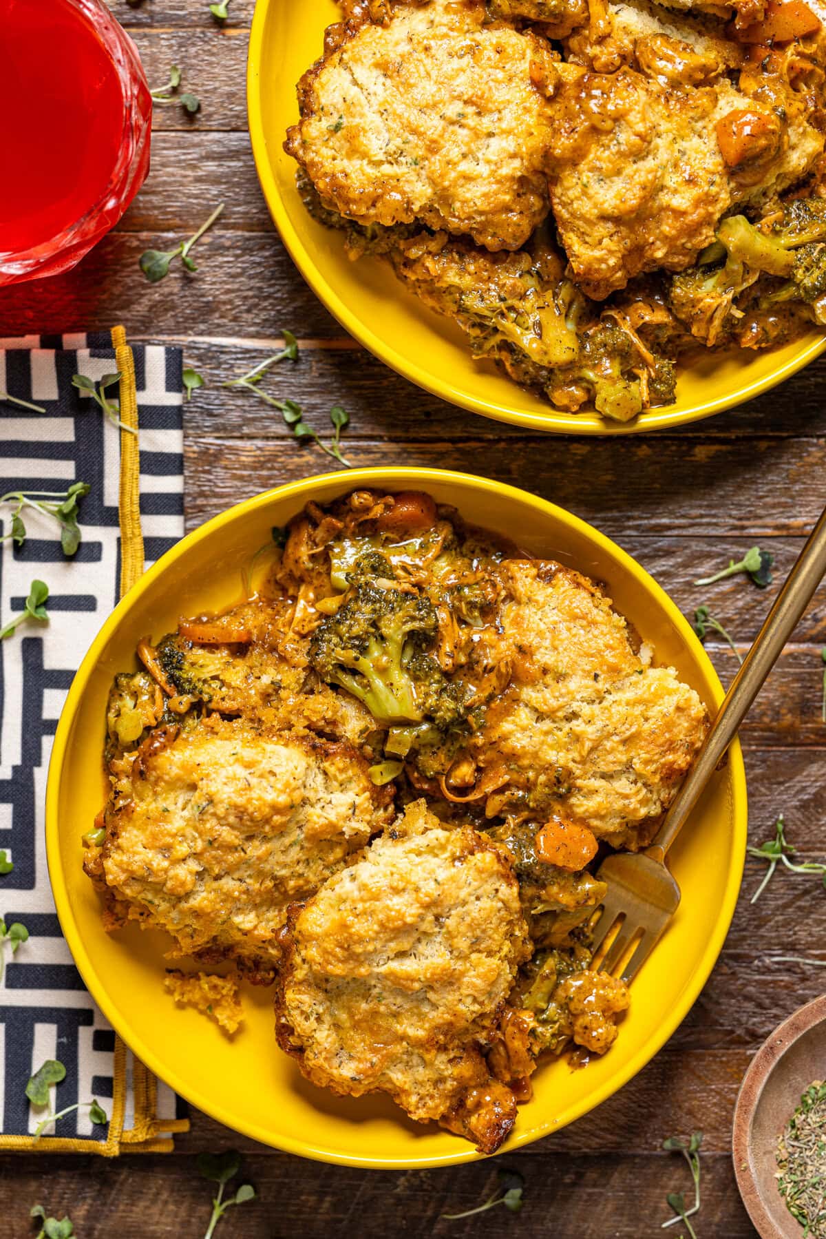 Two plates of broccoli cheddar pot pie with a fork and a drink.