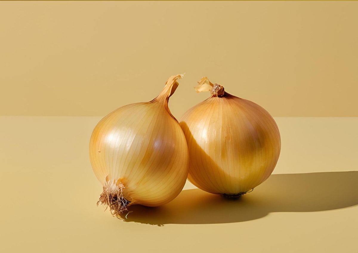 Two yellow onions on a tan background.