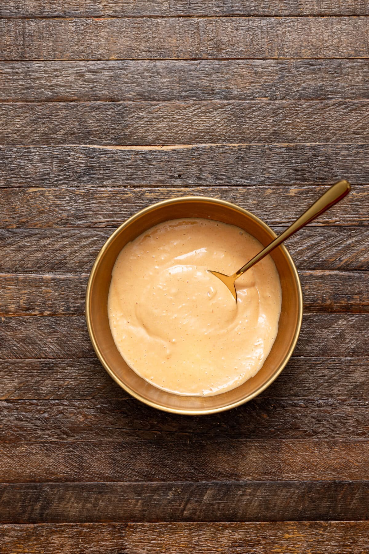 Dressing ingredients mixed together in a gold bowl with a spoon.