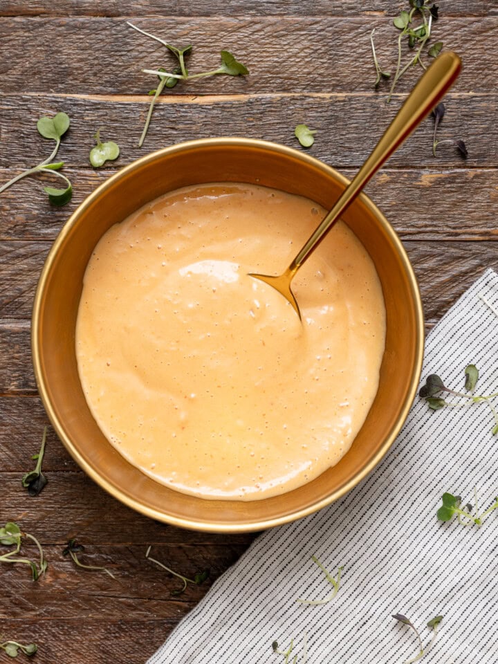 Dressing in a bowl on a brown wood table with a spoon.