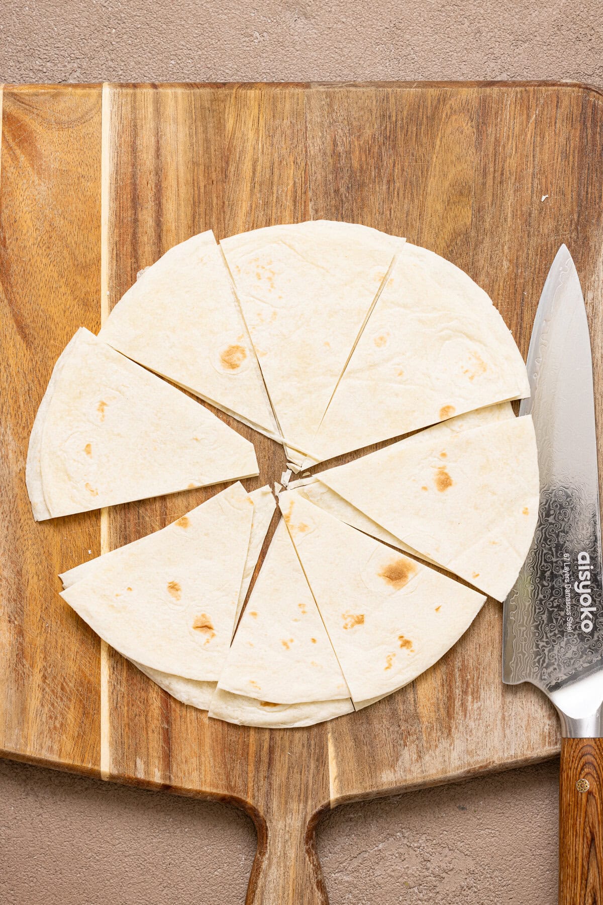 Flour tortillas sliced on a cutting board with a knife.