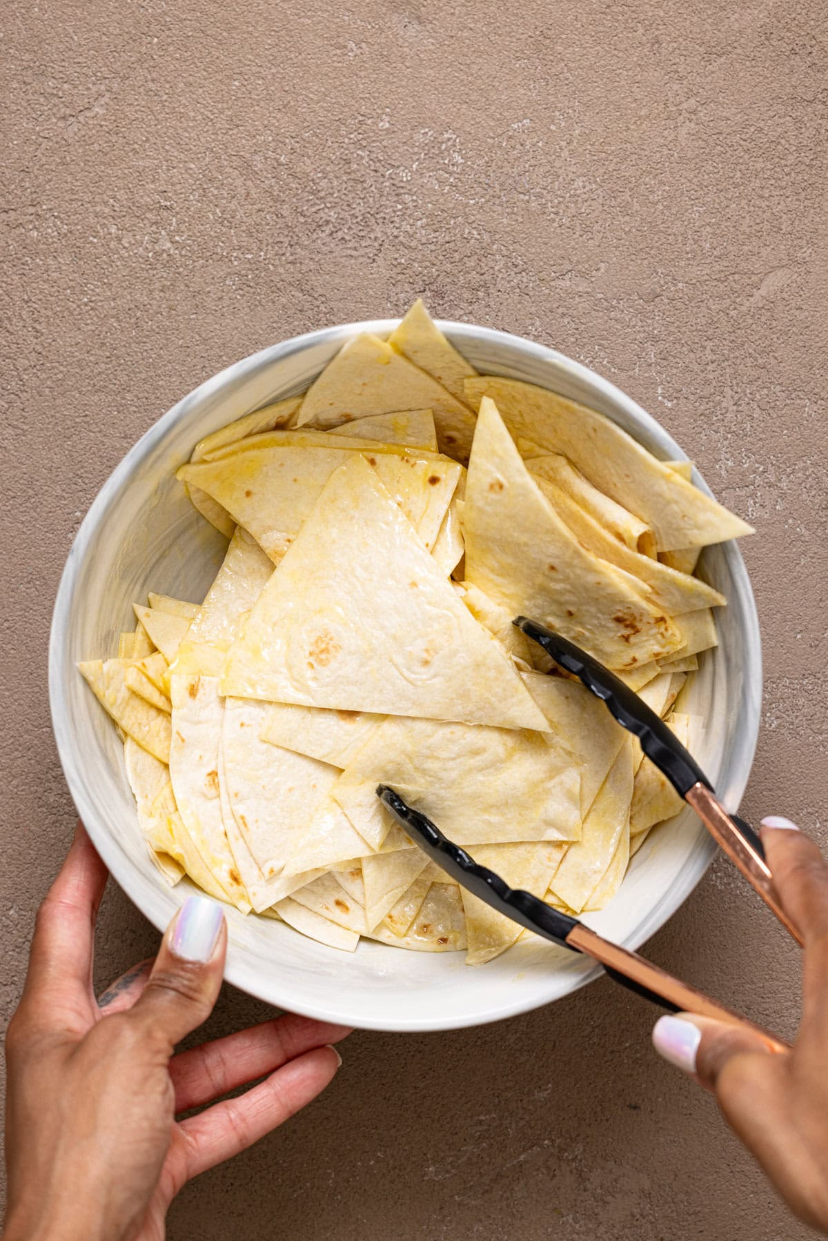 Sliced tortillas in a bowl being stirred with butter. 