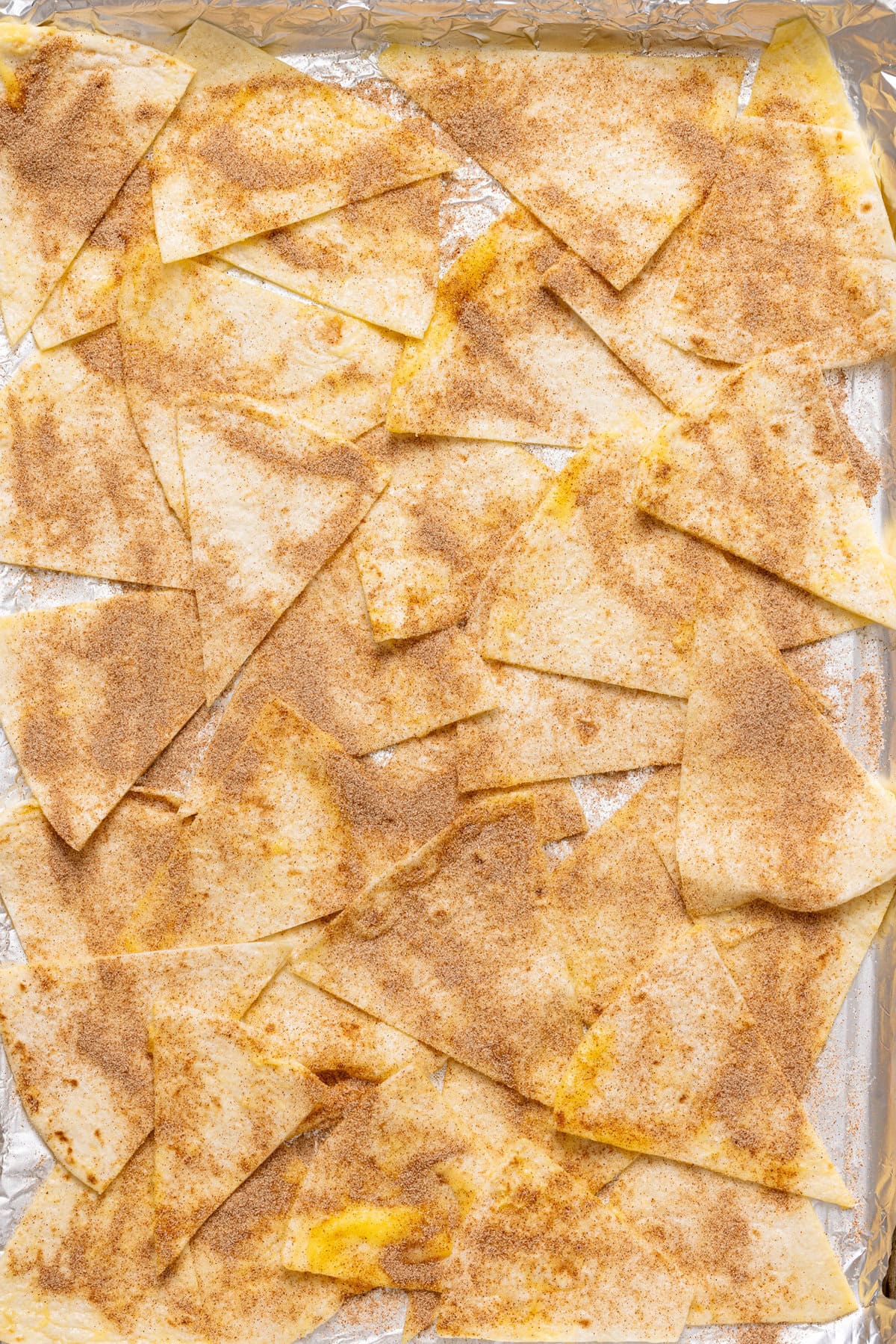 Tortillas slices on a baking sheet with sprinkles of cinnamon sugar.