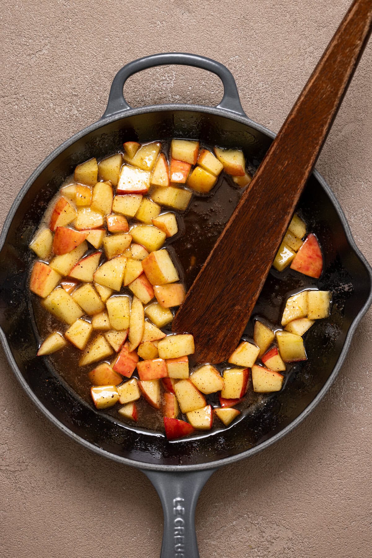 Sautéed apples in a skillet with a wooden spatula.