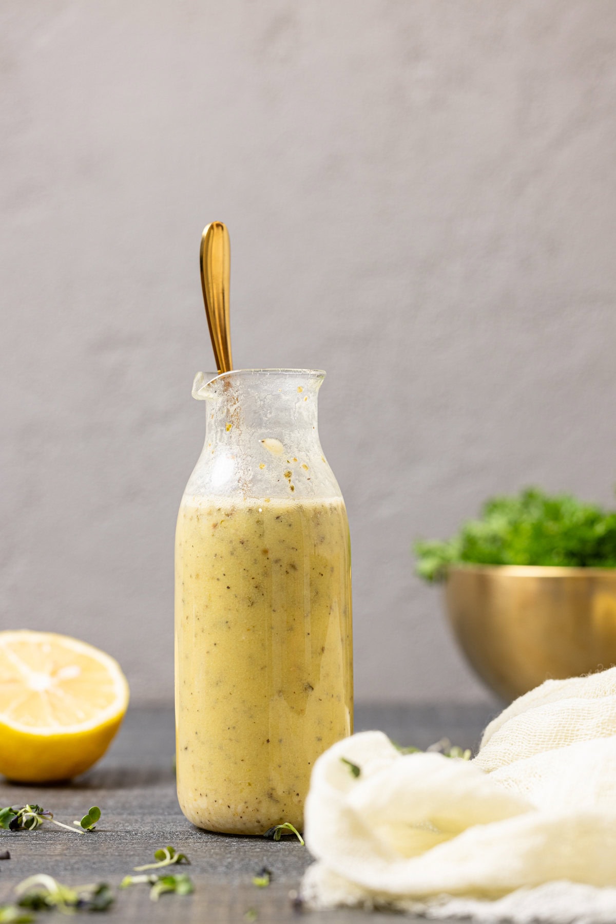 Dressing in a jar with a spoon and a lemon and herbs in the background.